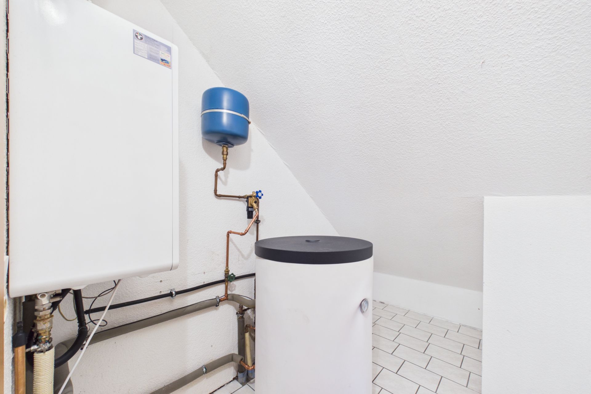 Hauswirtschaftsraum mit Heizungsanlage, Boiler und blauer Ausgleichsbehälter unter Dachschräge.