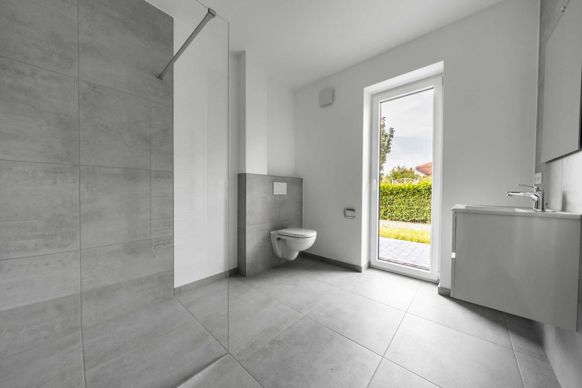 Modernes Badezimmer mit bodengleicher Dusche, WC, Waschbecken und einer Tür nach draußen.