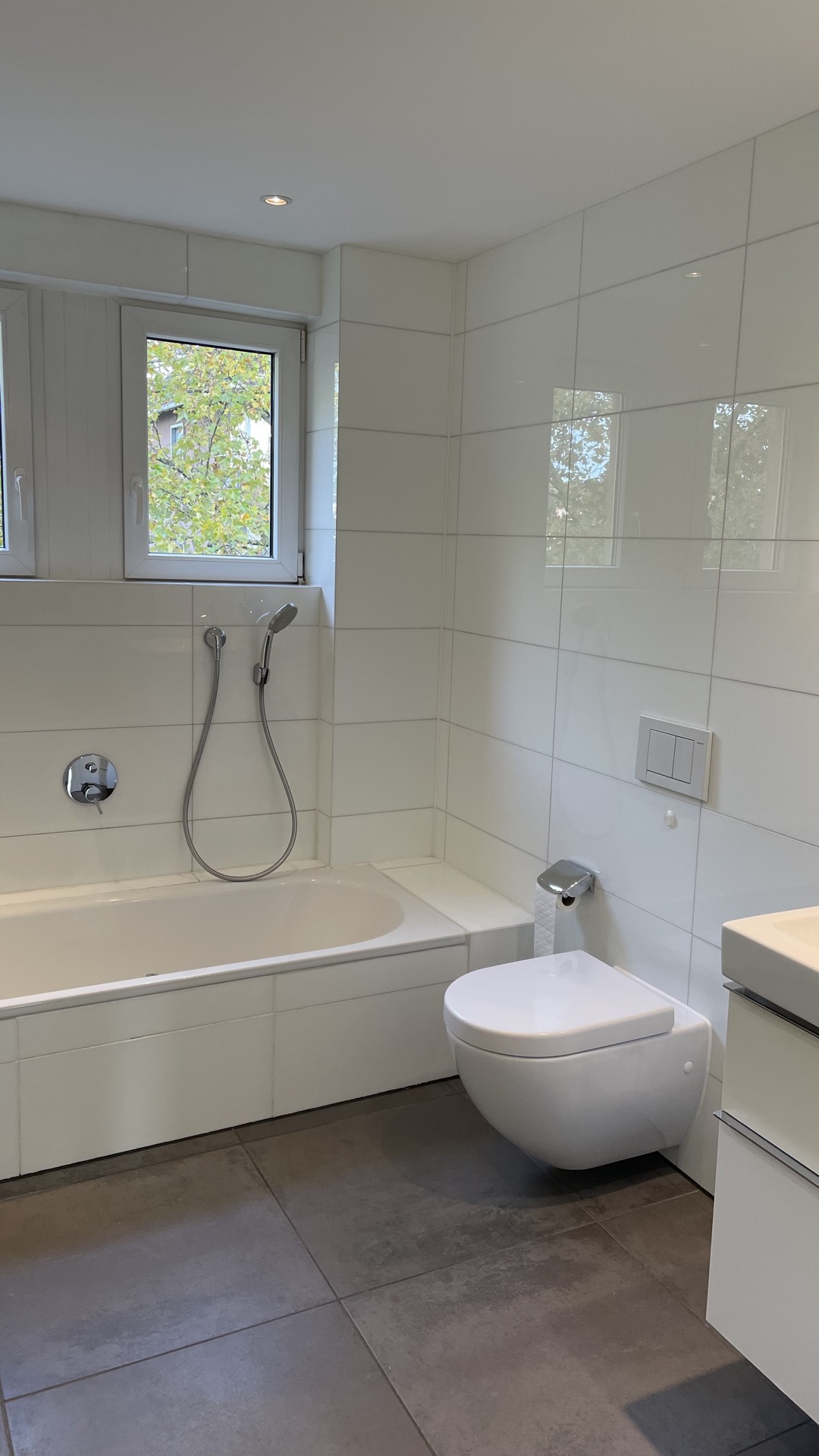 Modernes Bad mit Badewanne, Wandtoilette, Waschbecken und zwei Fenstern.