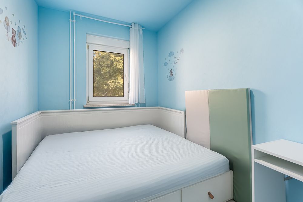 Kleines Schlafzimmer mit blau gestrichenen Wänden, einem Bett und einem Fenster.