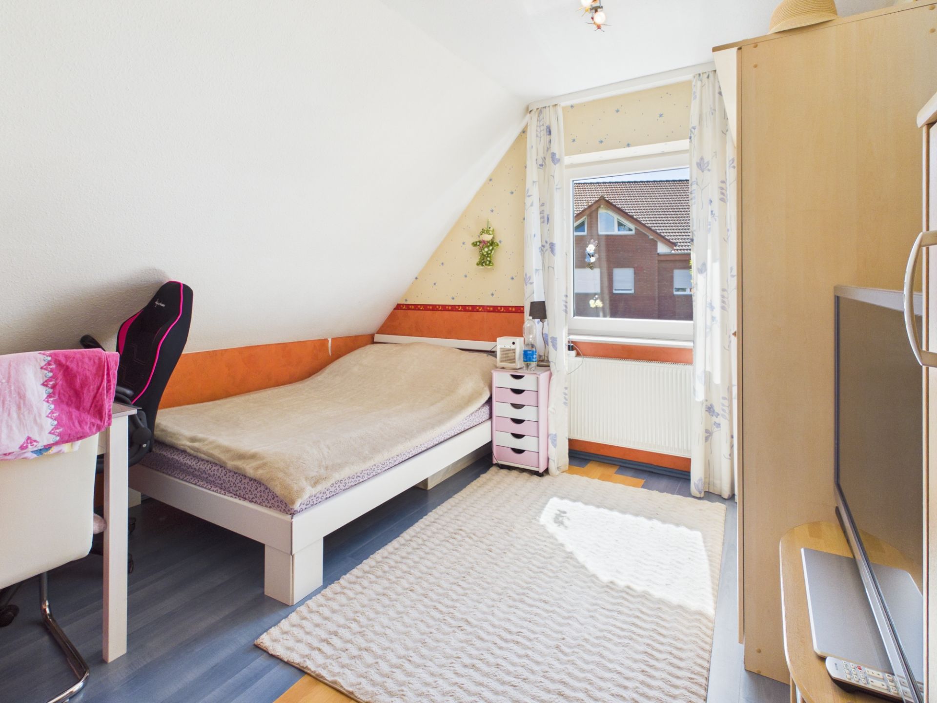 Helles Schlafzimmer mit Einzelbett, Schreibtisch, Teppich und Fenster mit Blick nach draußen.