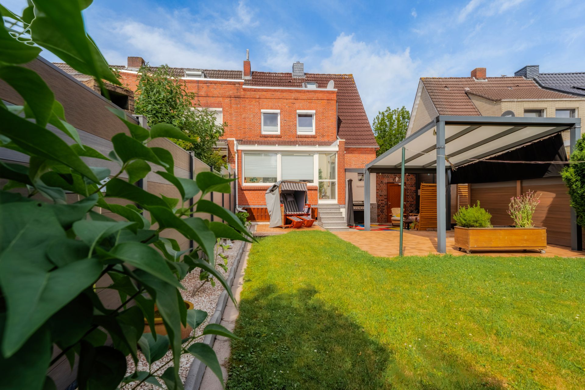 Gepflegter Garten mit Terrasse, Sitzbereich und Sicht auf ein rotes Backsteinhaus.
