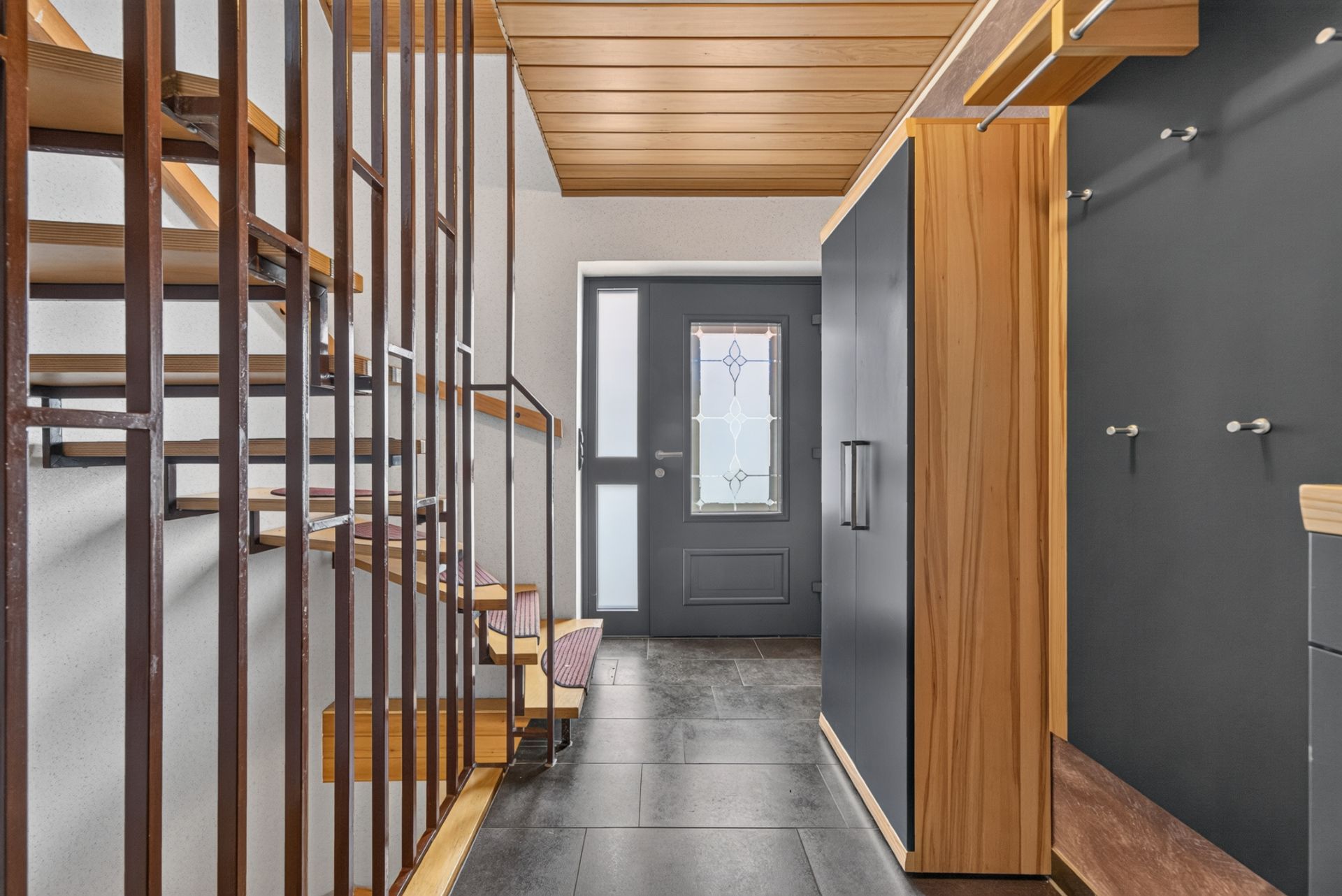 Moderner Flur mit dunkler Eingangstür, Holztreppe und Garderobe.