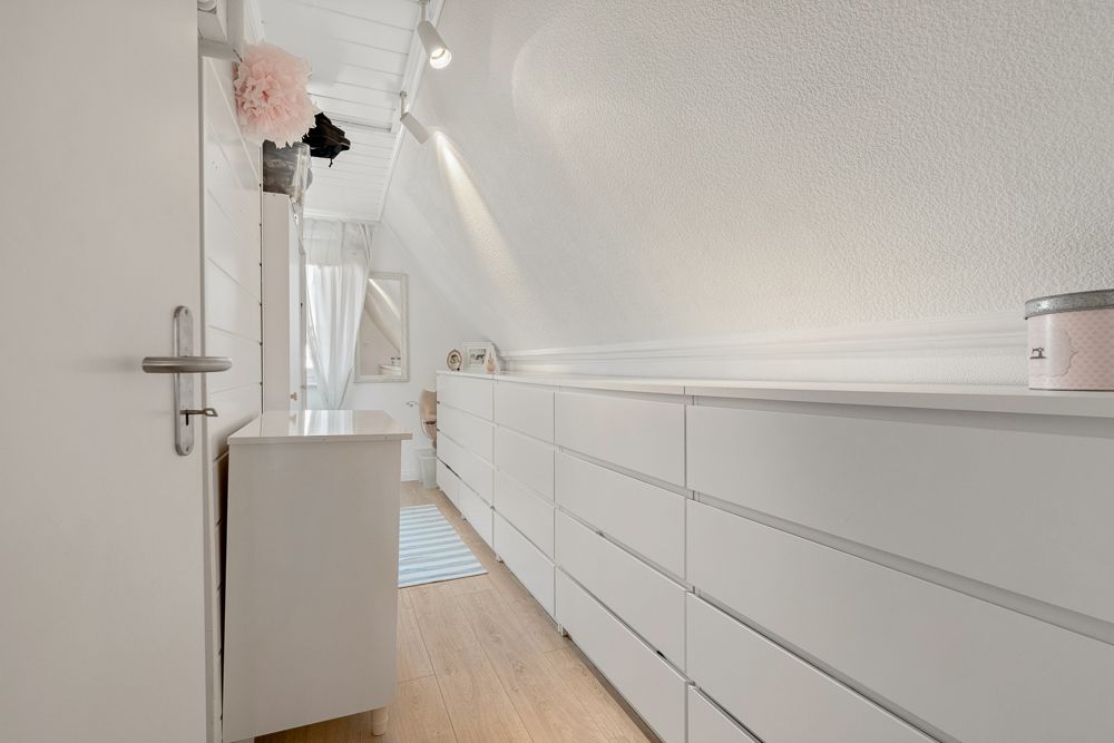 Heller Flur mit weißen Kommoden und Holzfußboden, Tageslicht kommt durch ein Fenster am Ende.