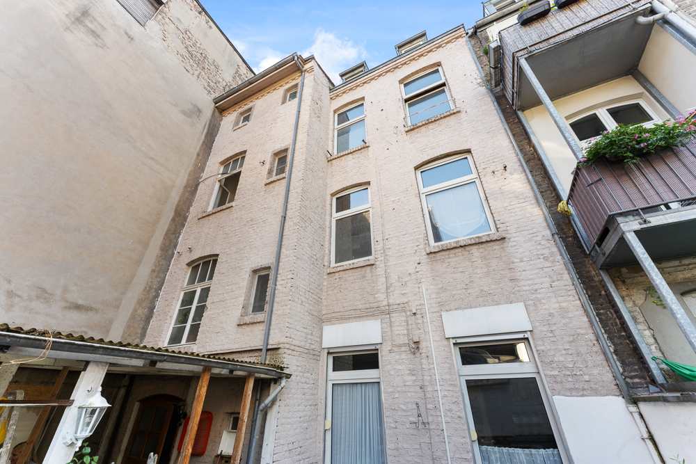 Heller Innenhof mit mehrstöckigem Wohngebäude und mehreren Fenstern sowie Balkon mit Blumen.
