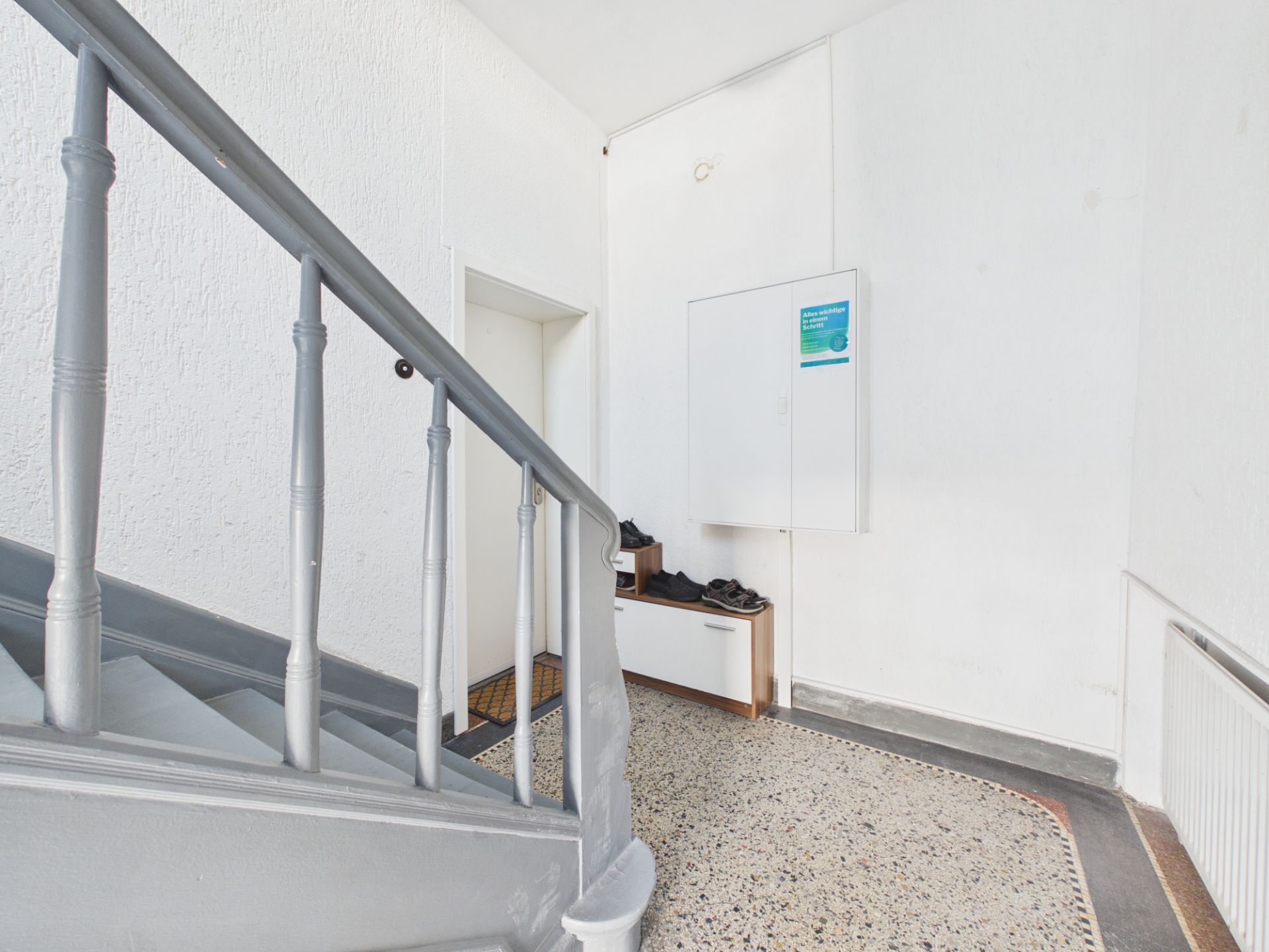 Heller Flur mit grauer Treppe, Schuhschrank und weißer Wand.