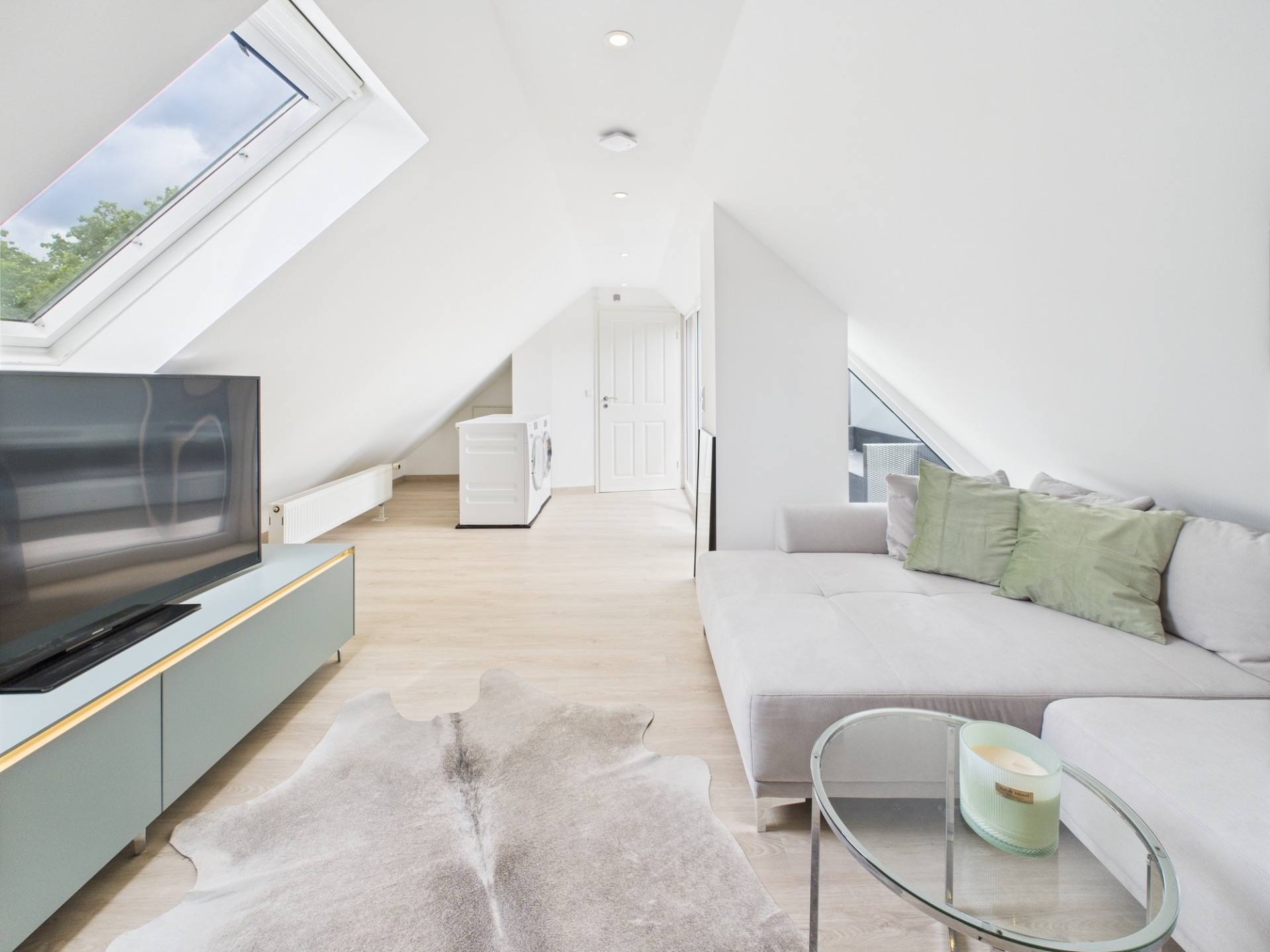 Helles Wohnzimmer mit Dachschrägen, Sofa, Fernseher und großen Fenstern.