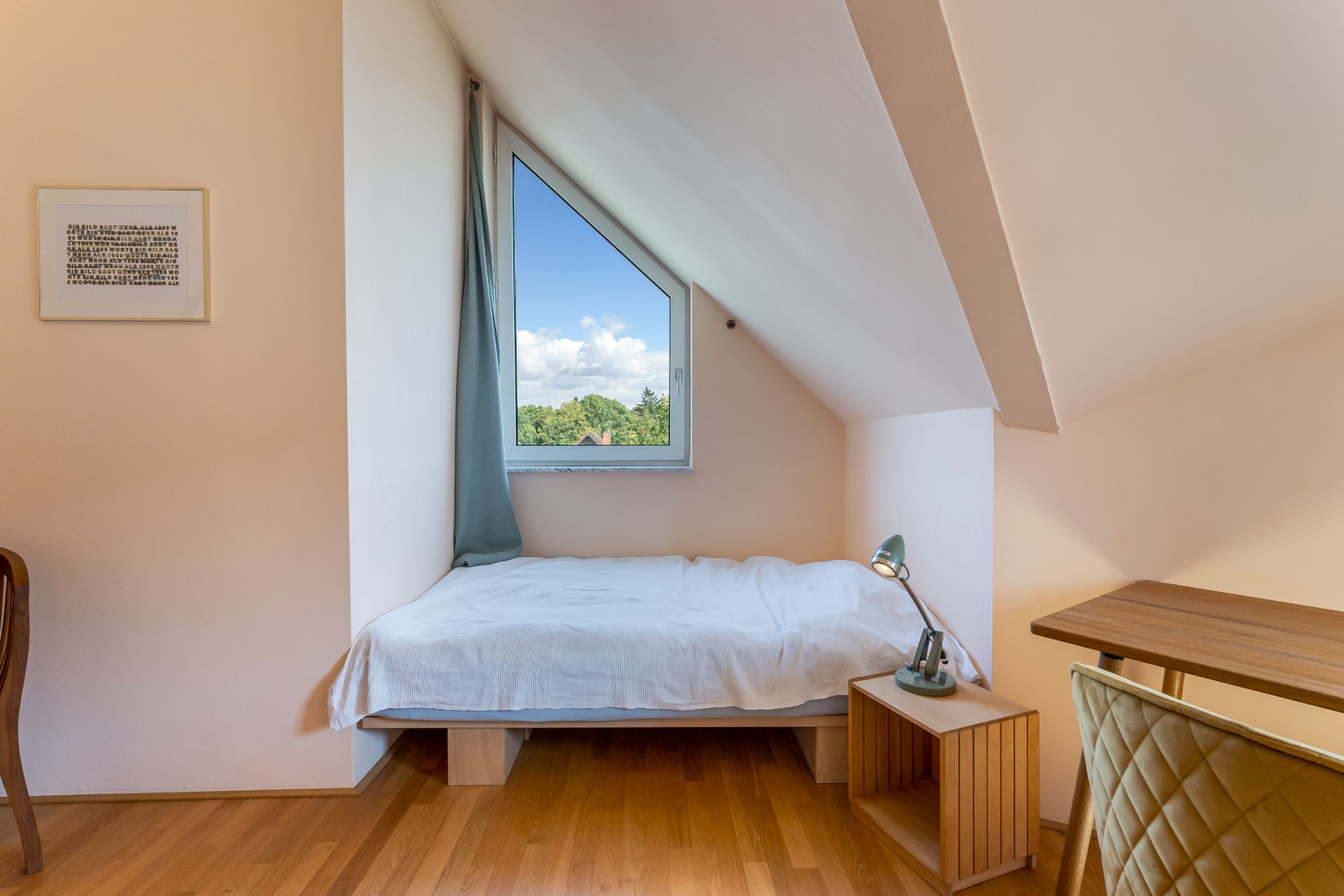 Helles Schlafzimmer mit Einzelbett, Schreibtisch und großem Fenster unter einer Dachschräge.