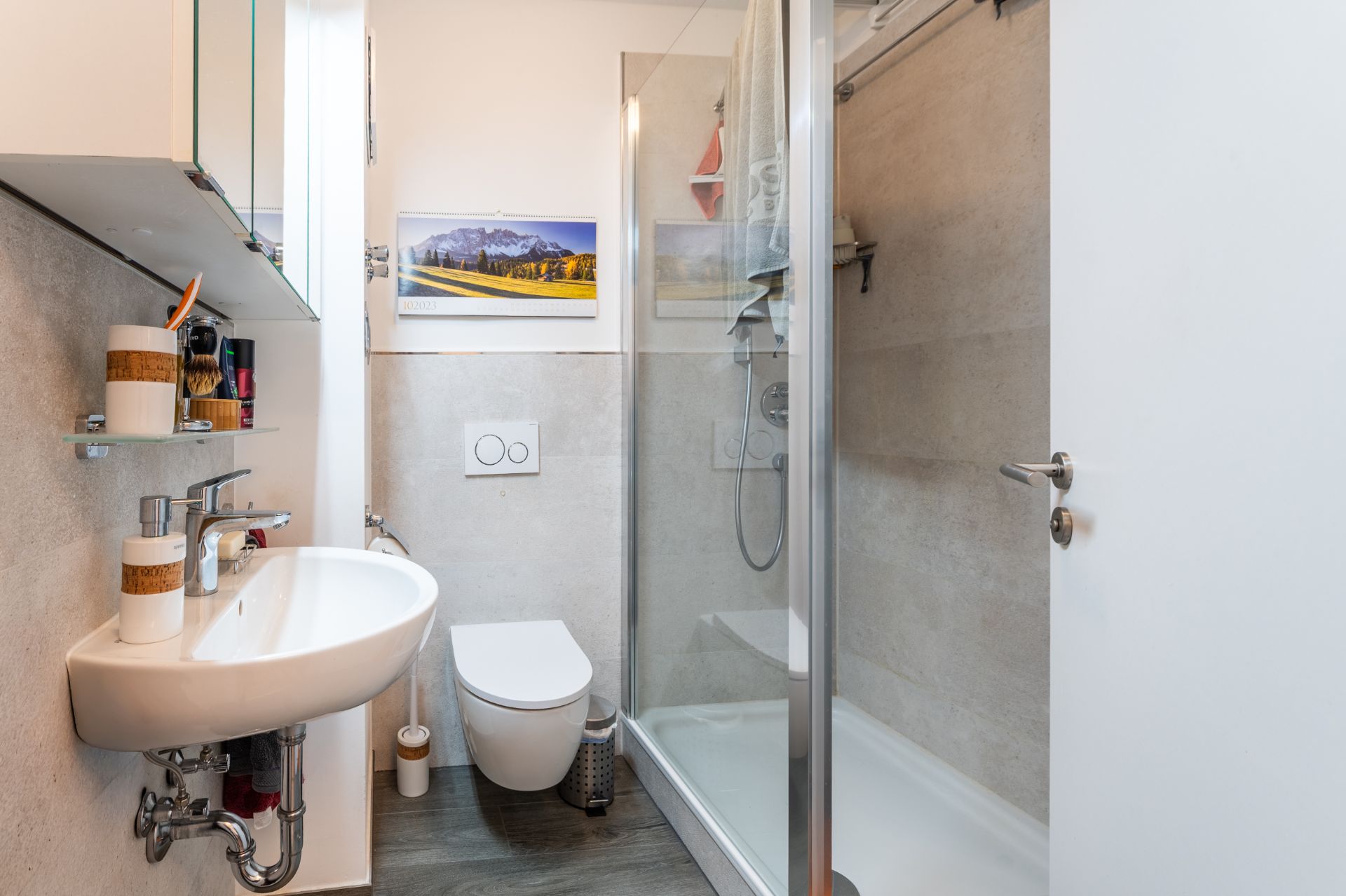 Modernes, kleines Bad mit Waschbecken, Toilette, Glasdusche und Bild an der Wand.