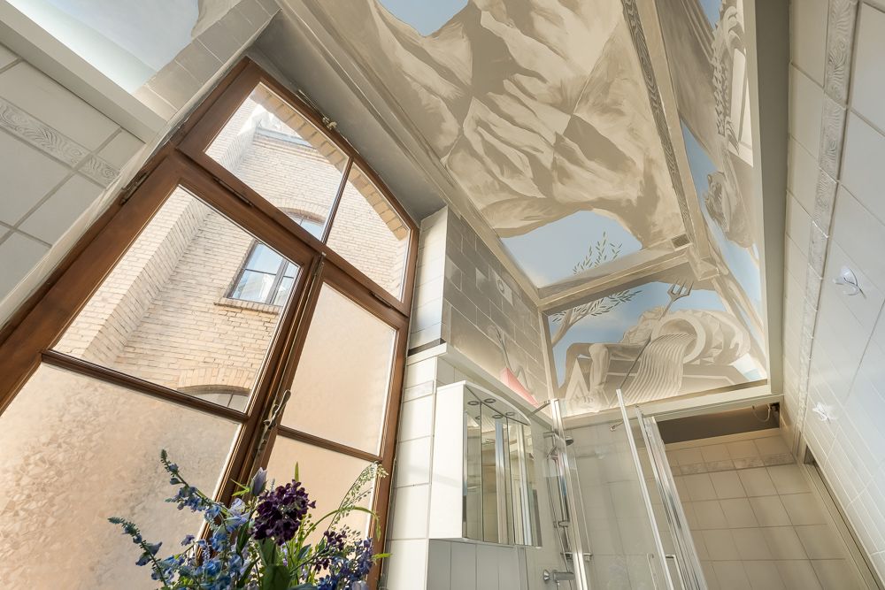 Badezimmer mit großem Fenster, Duschkabine und Deckenmalerei mit Bergmotiv.