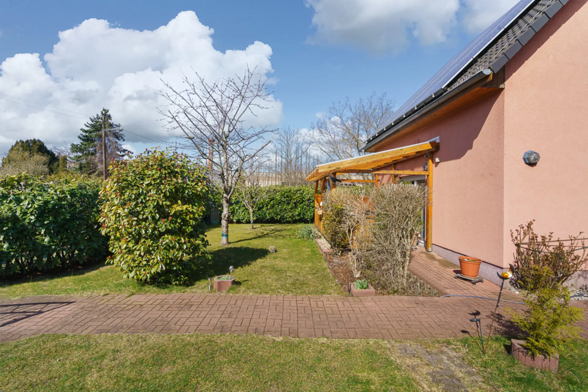 Garten mit Rasen, Sträuchern, Bäumen und Terrasse am Haus mit Solarpaneelen.