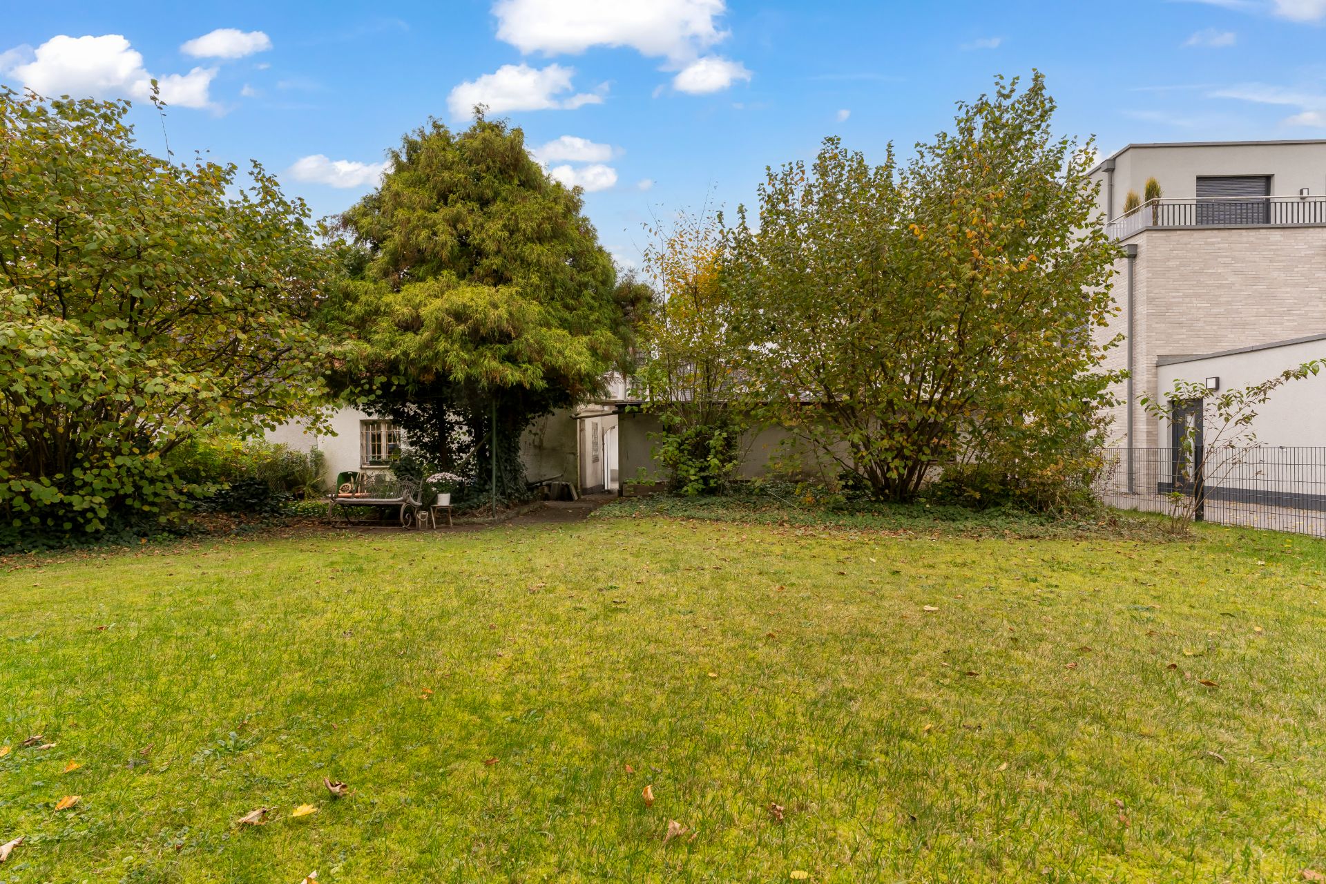 Großer Garten mit Rasenfläche, Bäumen, Sträuchern und einer Bank vor einem Haus.