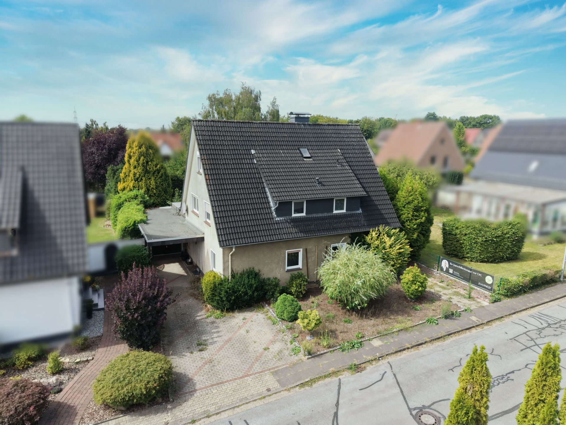 Einfamilienhaus mit dunklem Dach, Vorgarten und Einfahrt, umgeben von weiteren Häusern.