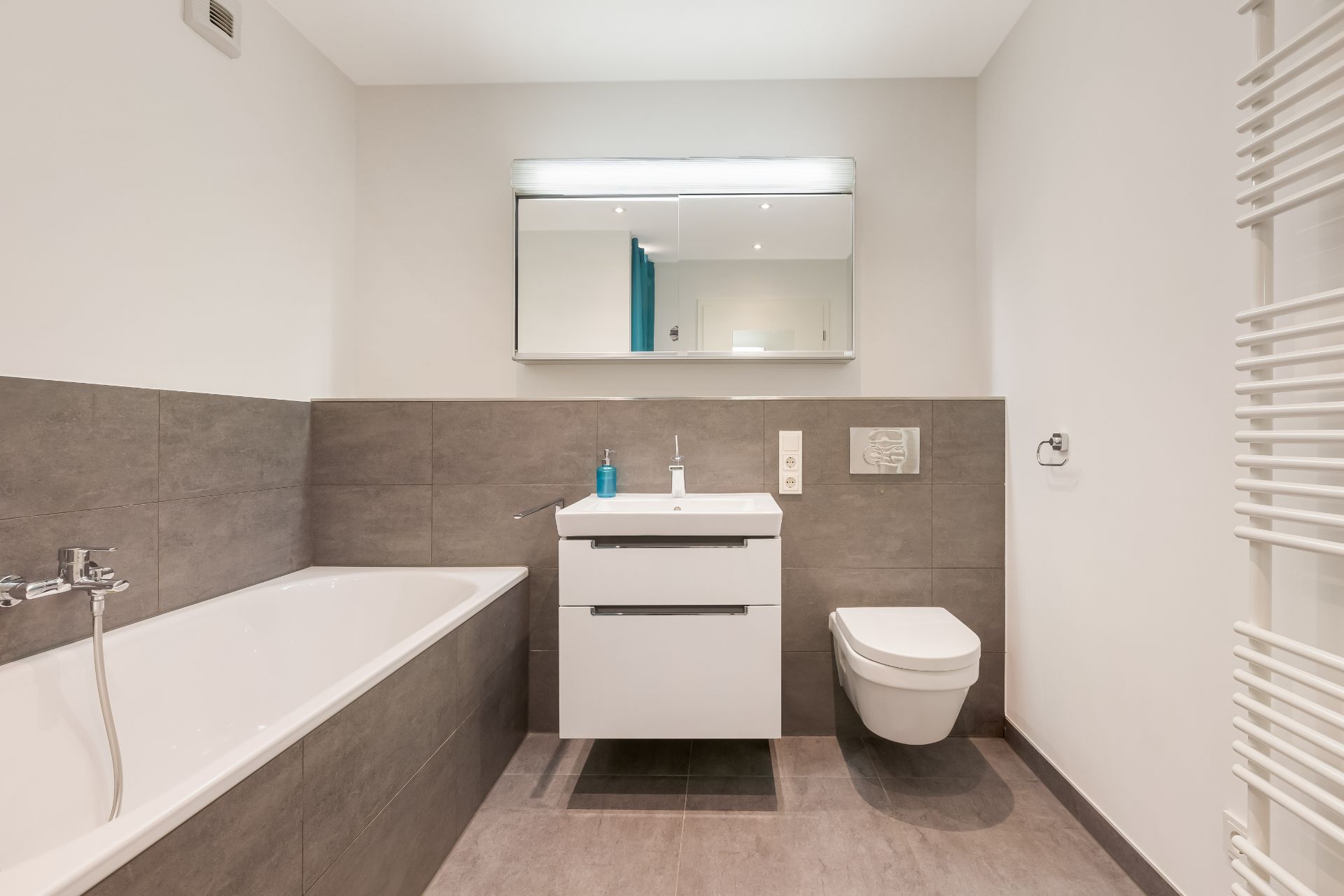 Modernes Badezimmer mit Badewanne, Waschbecken, Spiegel und wandhängendem WC.