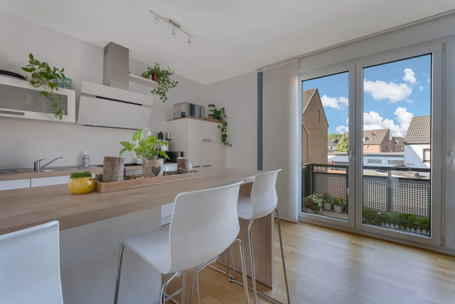 Moderne Küche mit Bartresen, weißen Stühlen, Pflanzen und großer Fensterfront mit Blick nach draußen.