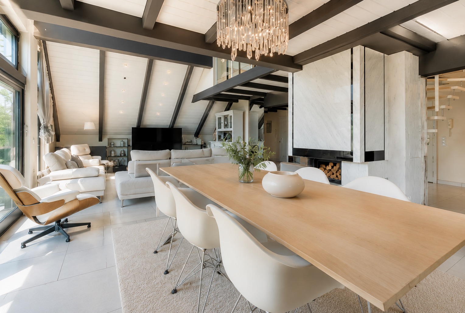 Helles Wohnzimmer mit Esstisch, weißen Stühlen, Sitzecke und großem Fenster.