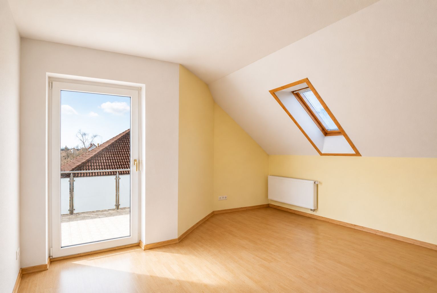 Helles Dachzimmer mit Laminatboden, Dachfenster, Tür zum Balkon und Heizkörper an der Wand.
