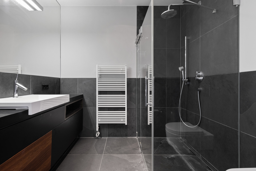 Modernes Bad mit Dusche, Waschbecken und Handtuchheizkörper, schwarze Fliesen.
