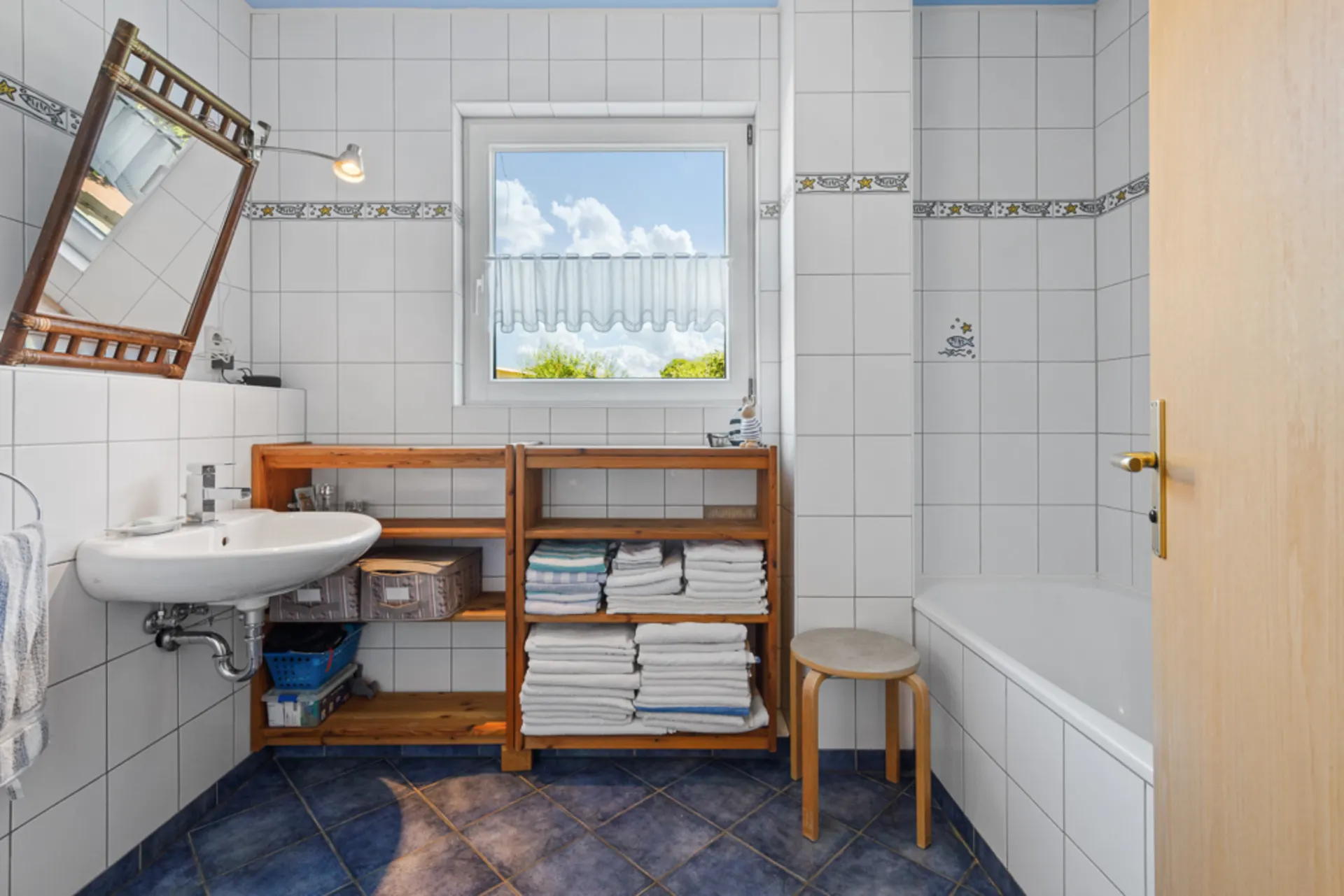 Helles Badezimmer mit Waschbecken, Badewanne, Regal mit Handtüchern und Fenster.