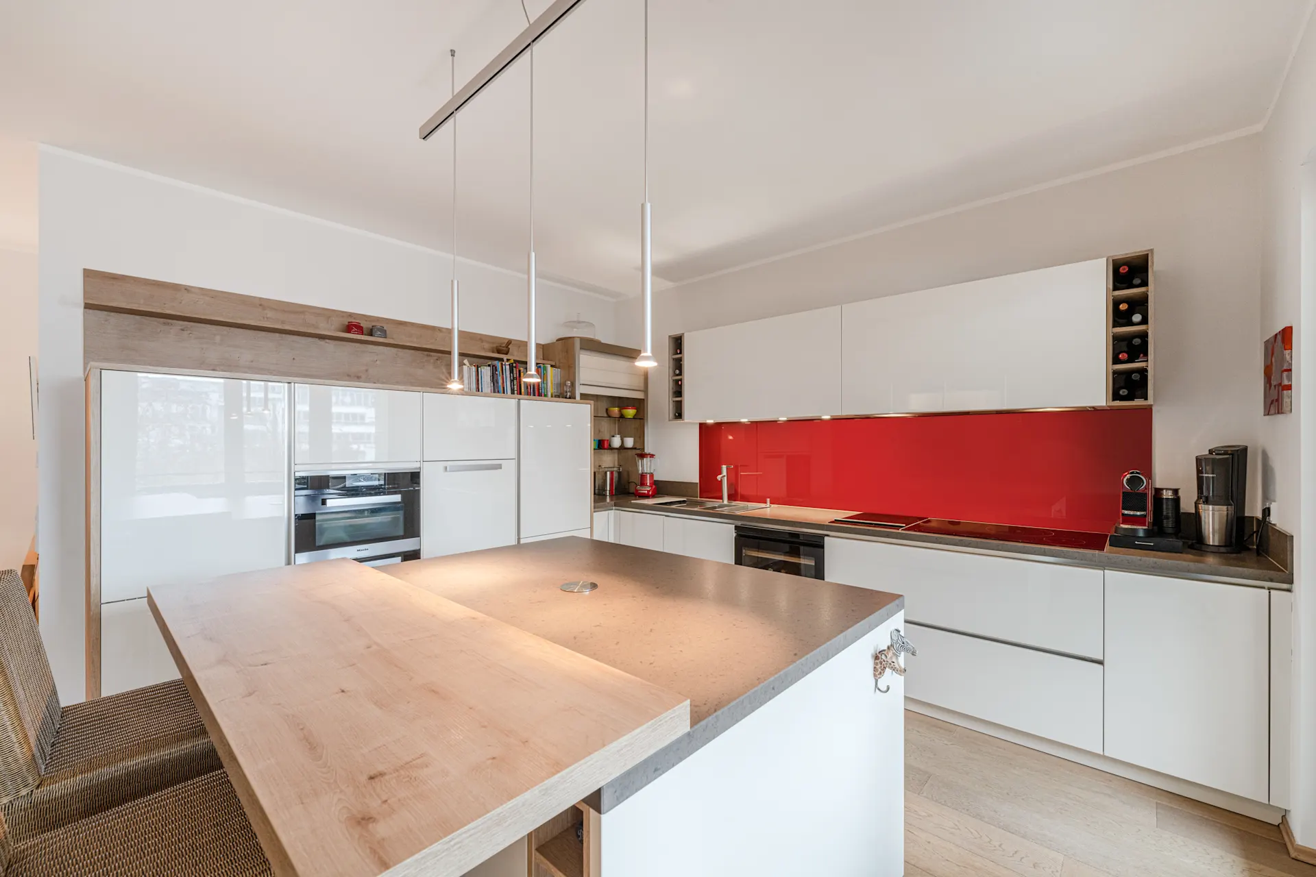 Moderne Küche mit roter Rückwand, weißem Mobiliar und Kochinsel mit Holzplatte.