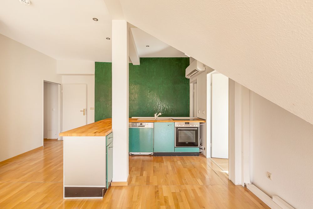 Moderne Küche mit Holzarbeitsplatte, grüner Wand und Einbaugeräten in einer Wohnung.