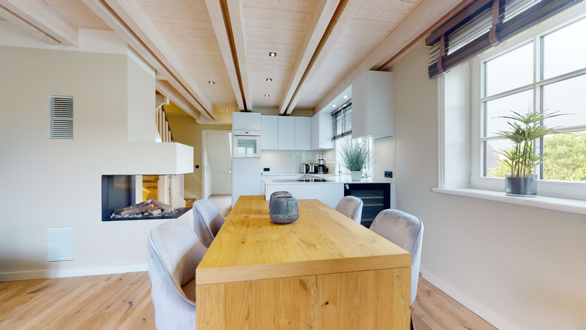 Helles Esszimmer mit Holztisch, sechs Stühlen, Kamin und Fenster mit Pflanzen.