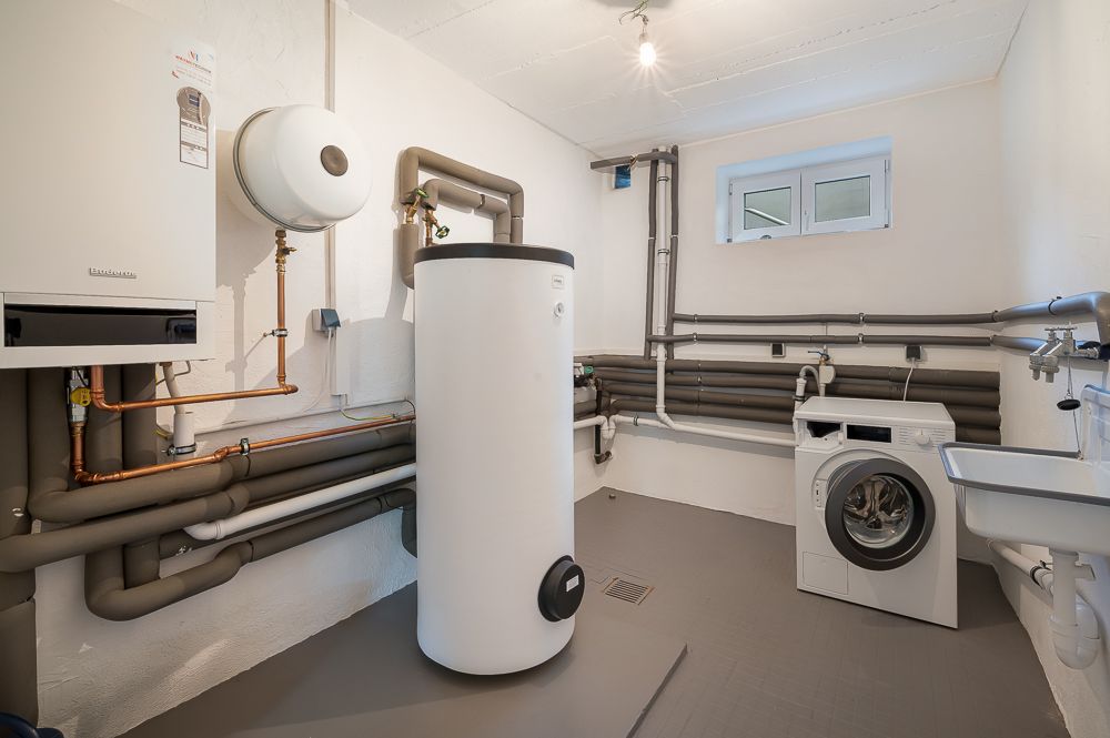 Waschküche mit Waschmaschine, großem Boiler, Wandheizung und Waschbecken.