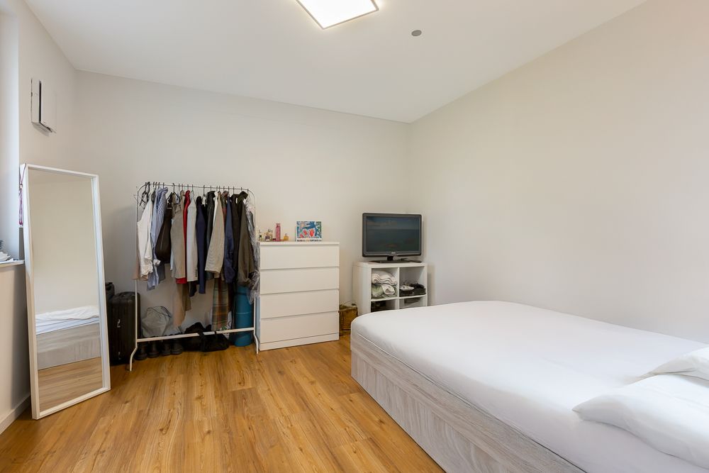 Helles Schlafzimmer mit Bett, Kommode, Kleiderständer und Spiegel auf Holzfußboden.