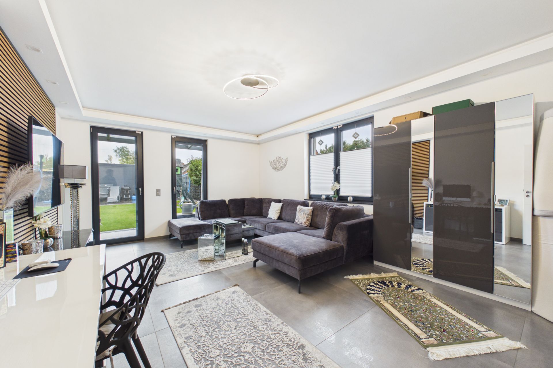 Modernes Wohnzimmer mit Ecksofa, Teppichen, Glastisch und Zugang zum Garten.