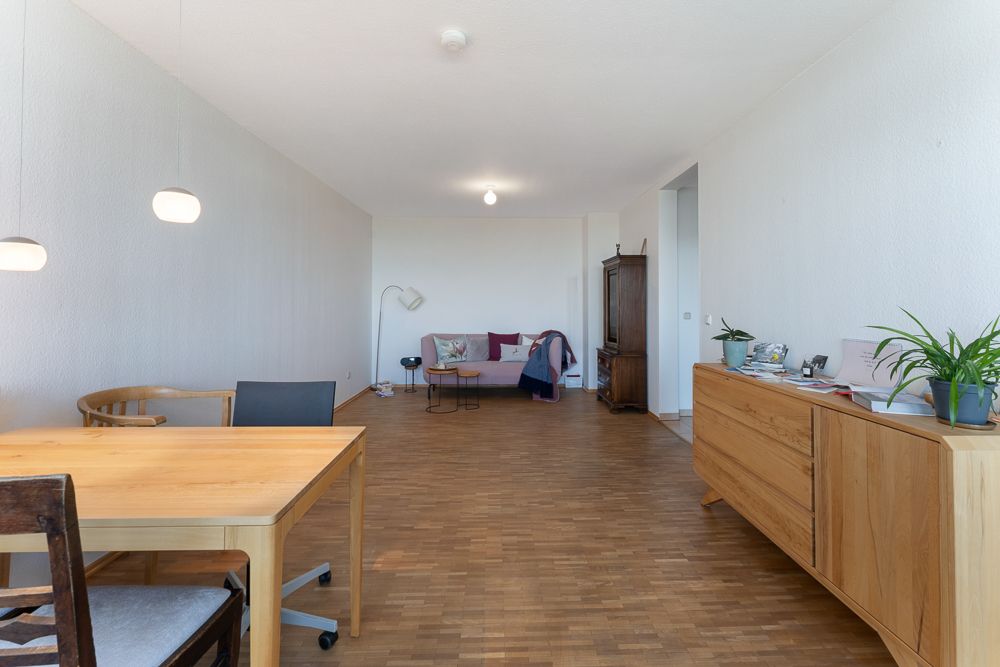 Helles Wohnzimmer mit Holzboden, Esstisch, Sideboard, Sofa und Stehlampe.