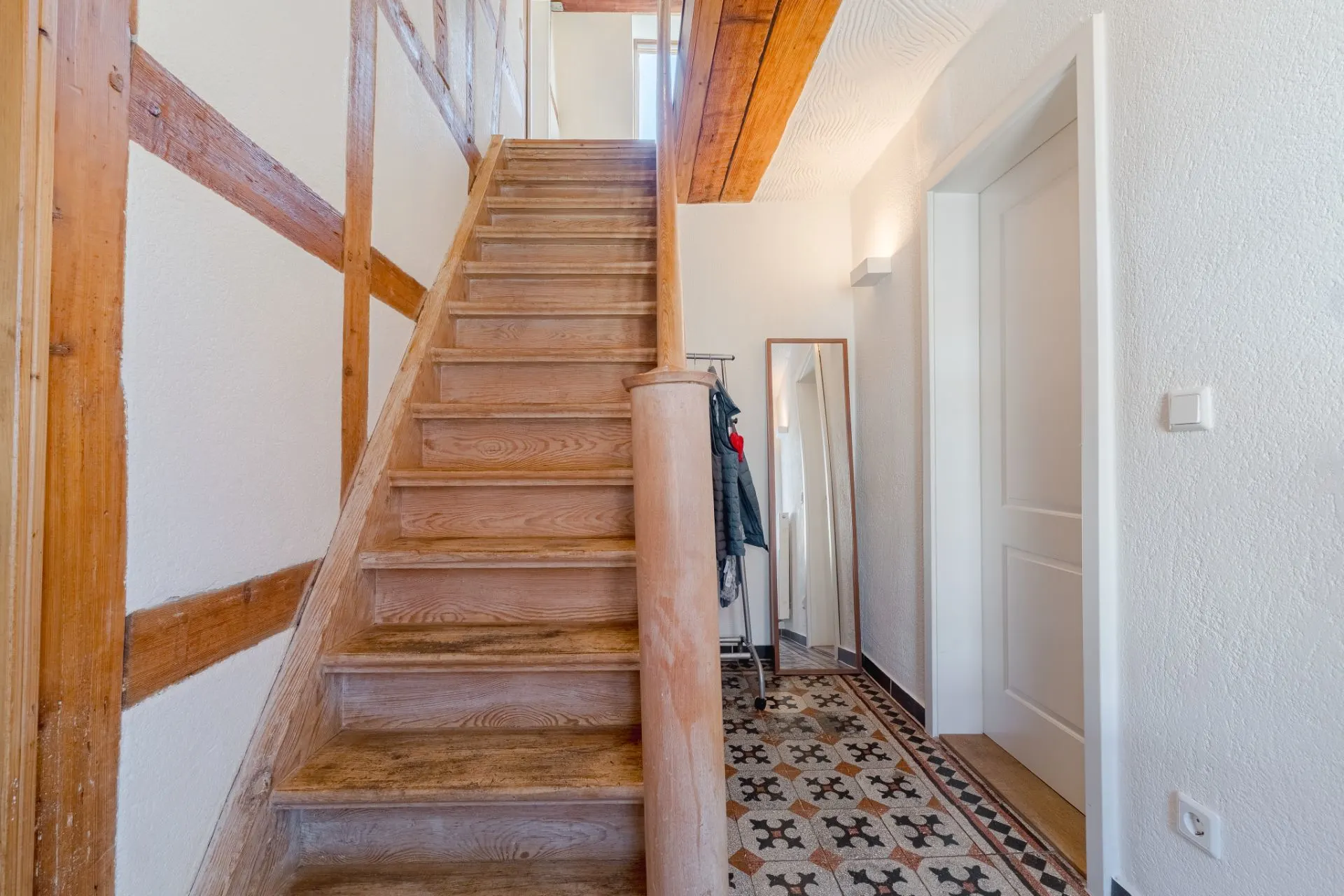 Holztreppe in einem Flur mit gemustertem Fliesenboden und einem Spiegel an der Wand.