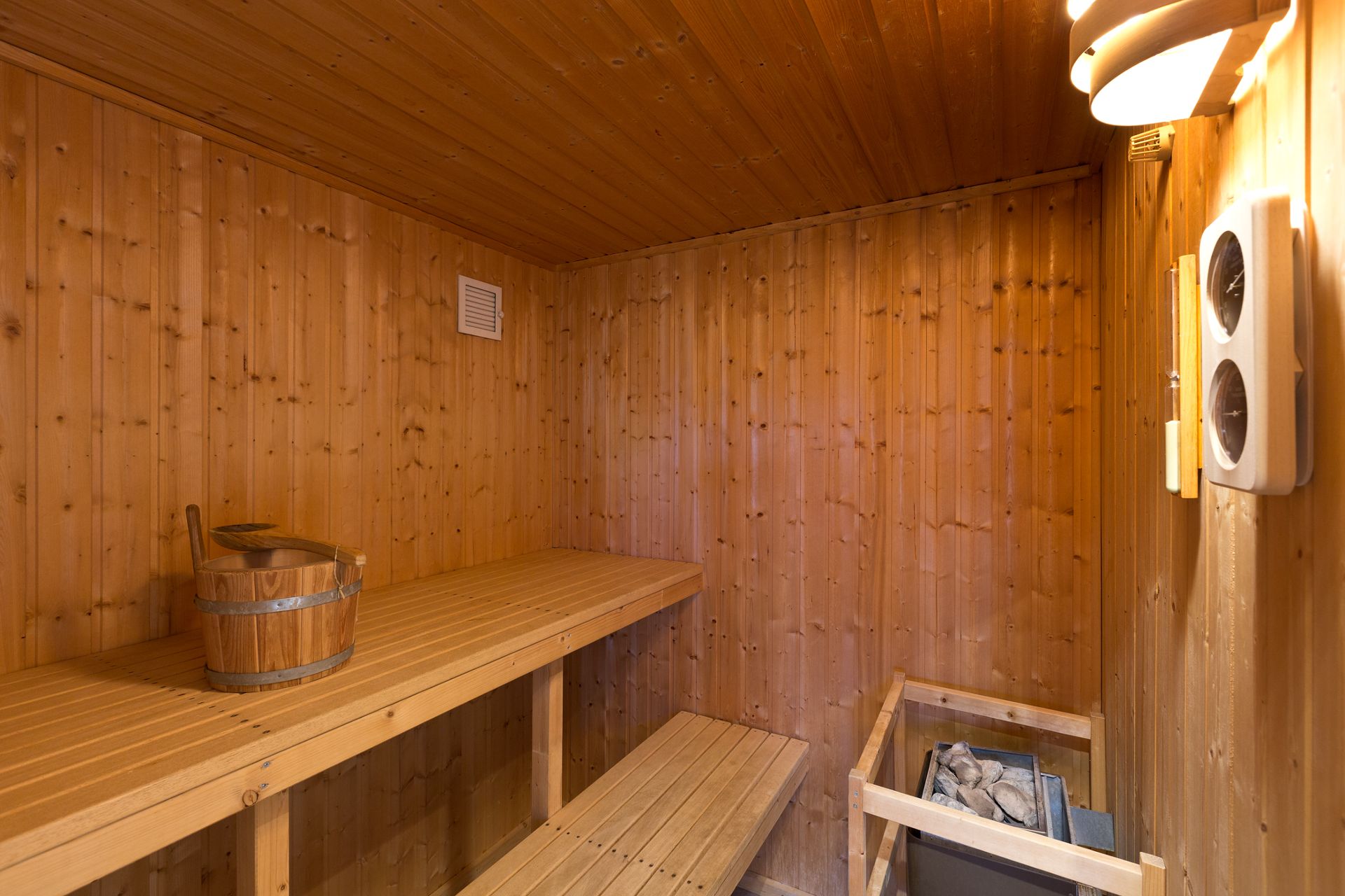 Holzsauna mit Bank, Saunasteinen und einem Holzeimer mit Schöpfkelle.