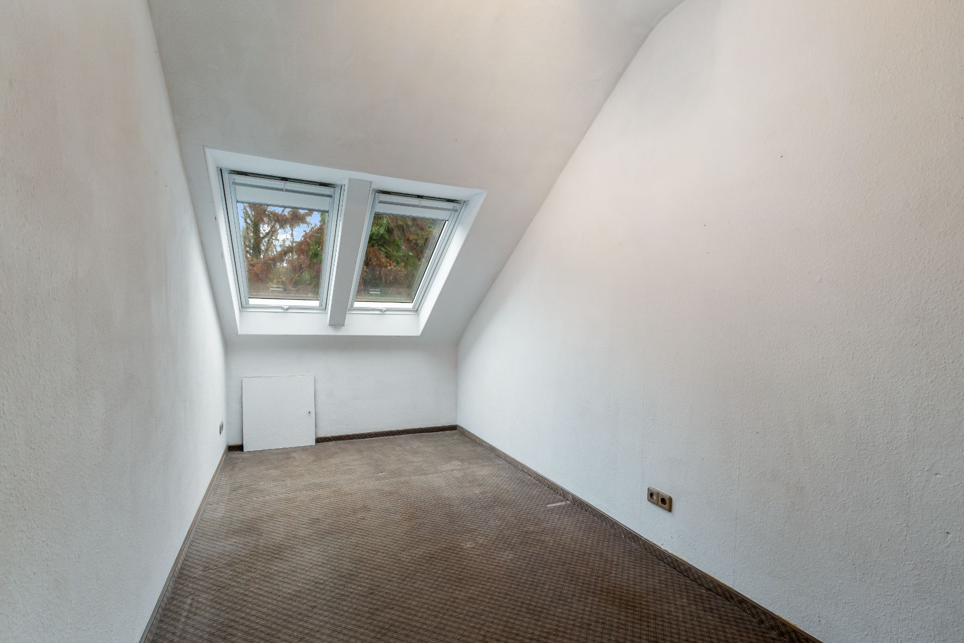 Leerer Raum mit zwei Dachfenstern und Teppichboden unter einer schrägen Decke.
