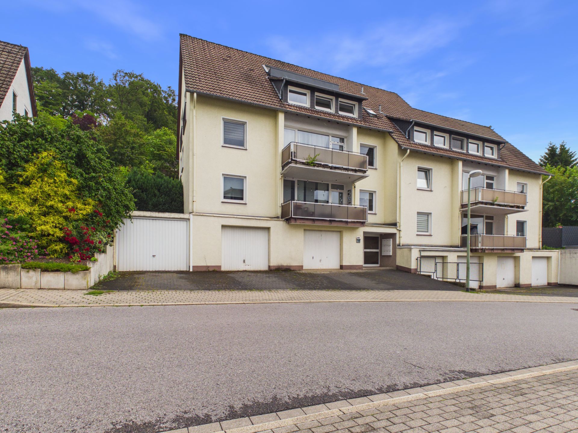 Mehrfamilienhaus mit Balkonen, Garagen und großer Einfahrt an einer ruhigen Straße.