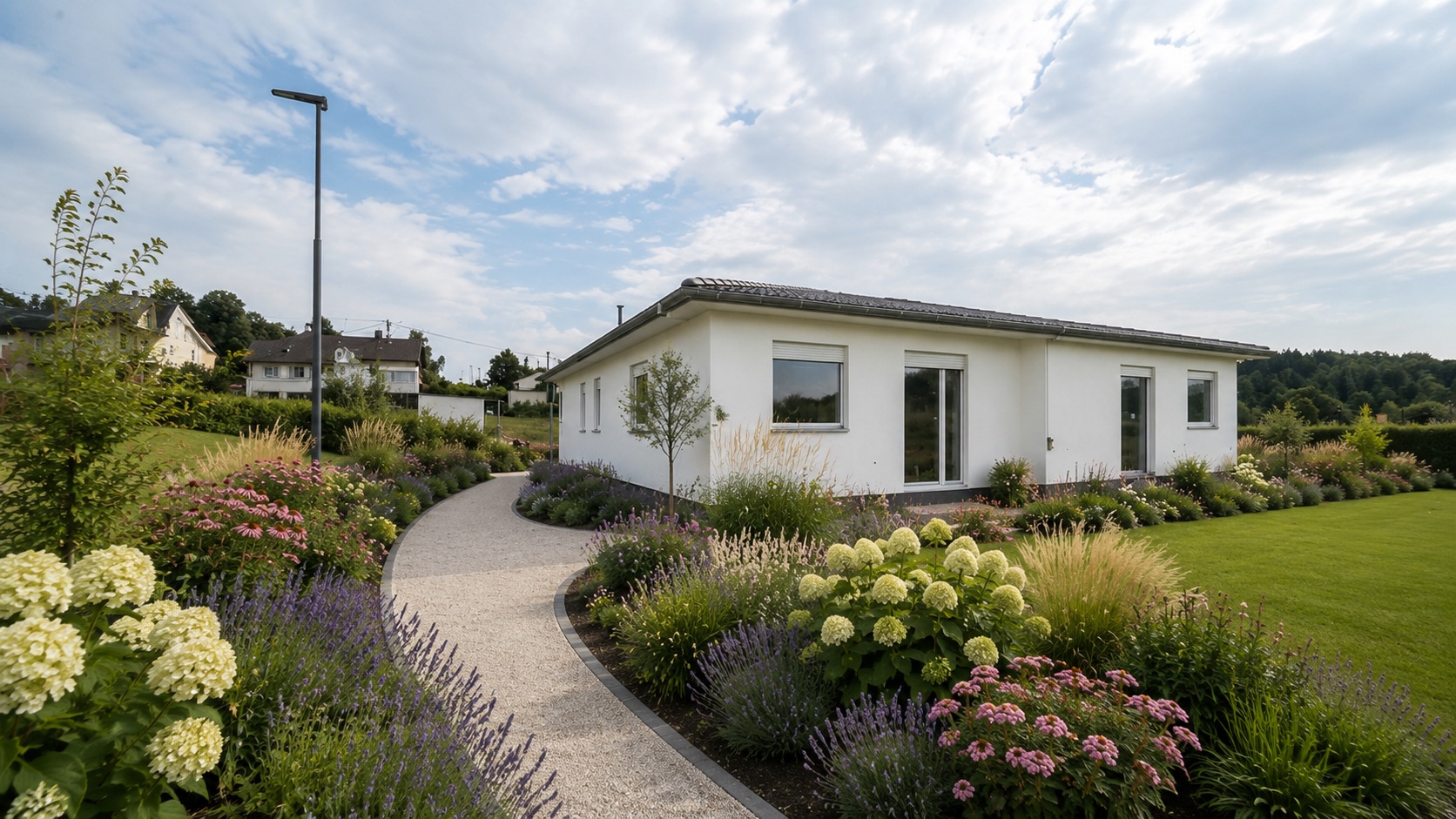 Weißes Einfamilienhaus mit großem Garten und blühenden Blumenbeeten bei Tageslicht.