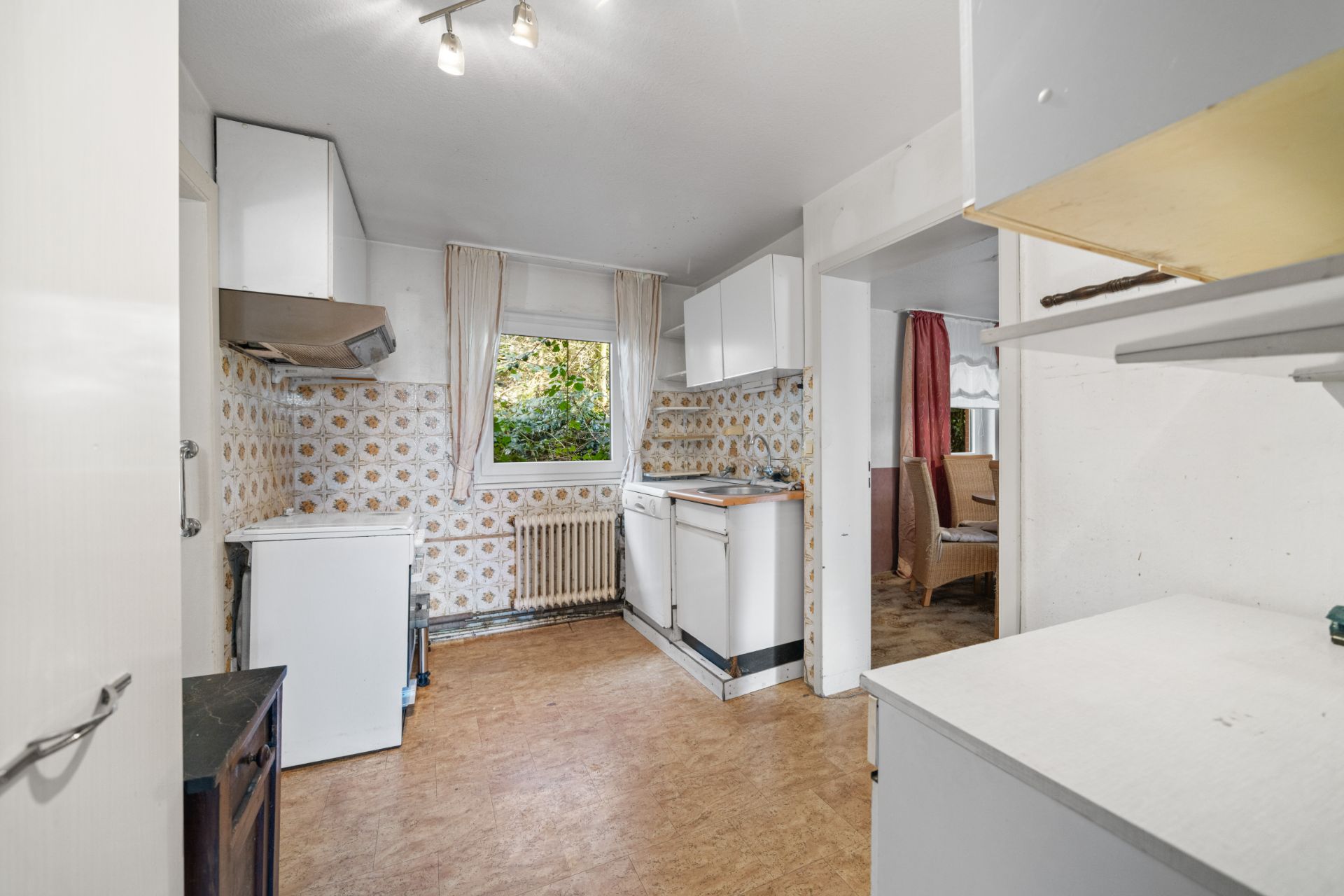 Helle Küche mit weißen Schränken, Fenster und gemusterten Fliesen an den Wänden.