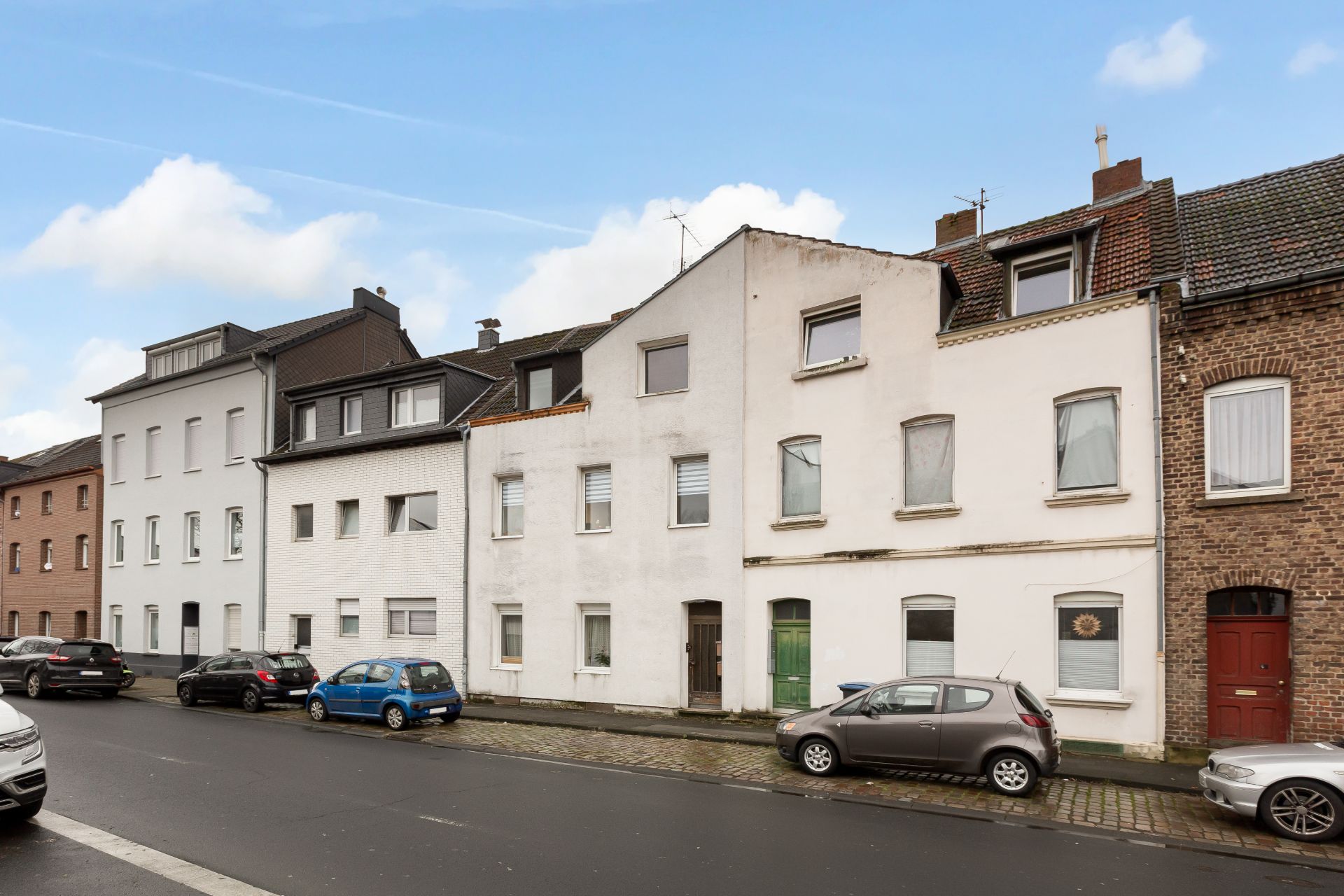 Reihe mehrstöckiger Wohnhäuser mit geparkten Autos entlang einer Straße.