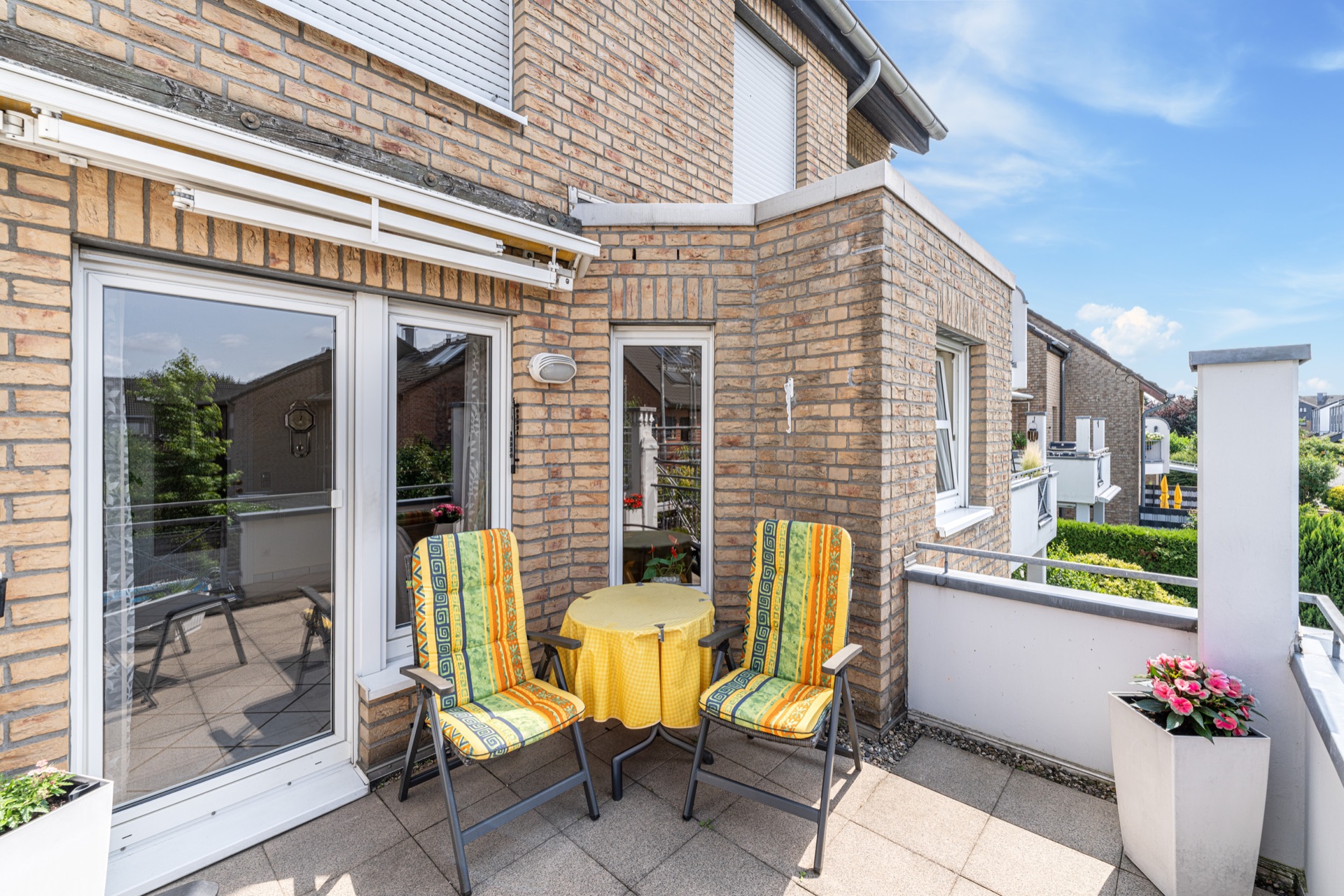 Balkon mit zwei bunten Stühlen, kleinem Tisch und Blumenkasten an einem Backsteinhaus.