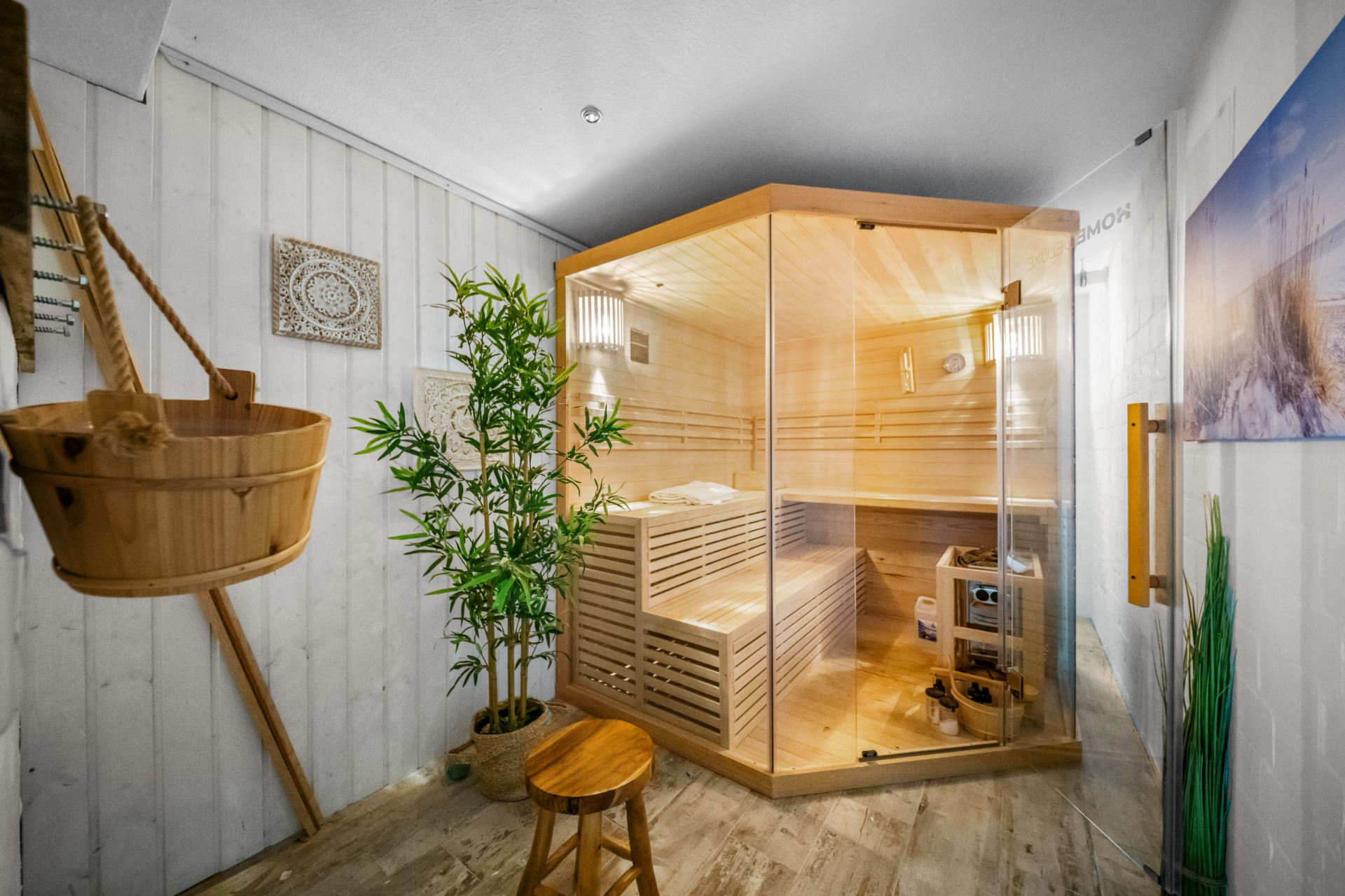 Heller Raum mit moderner Sauna aus Holz und Glas, Bambuspflanze und Holzhocker.