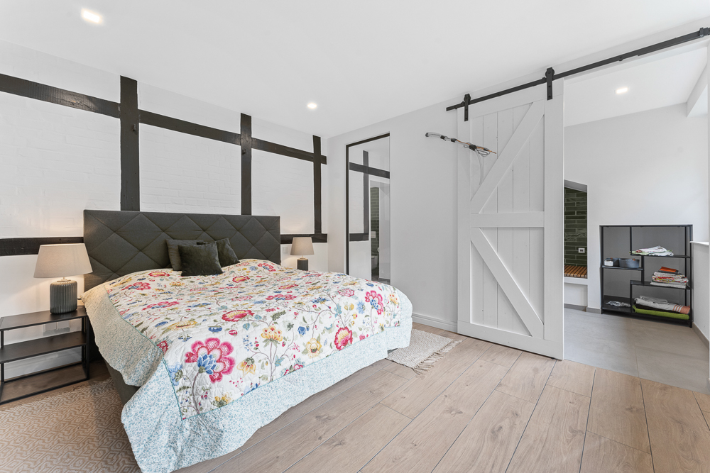 Modernes Schlafzimmer mit Doppelbett, Nachttischen, Schiebetür und Regal im Nebenraum.