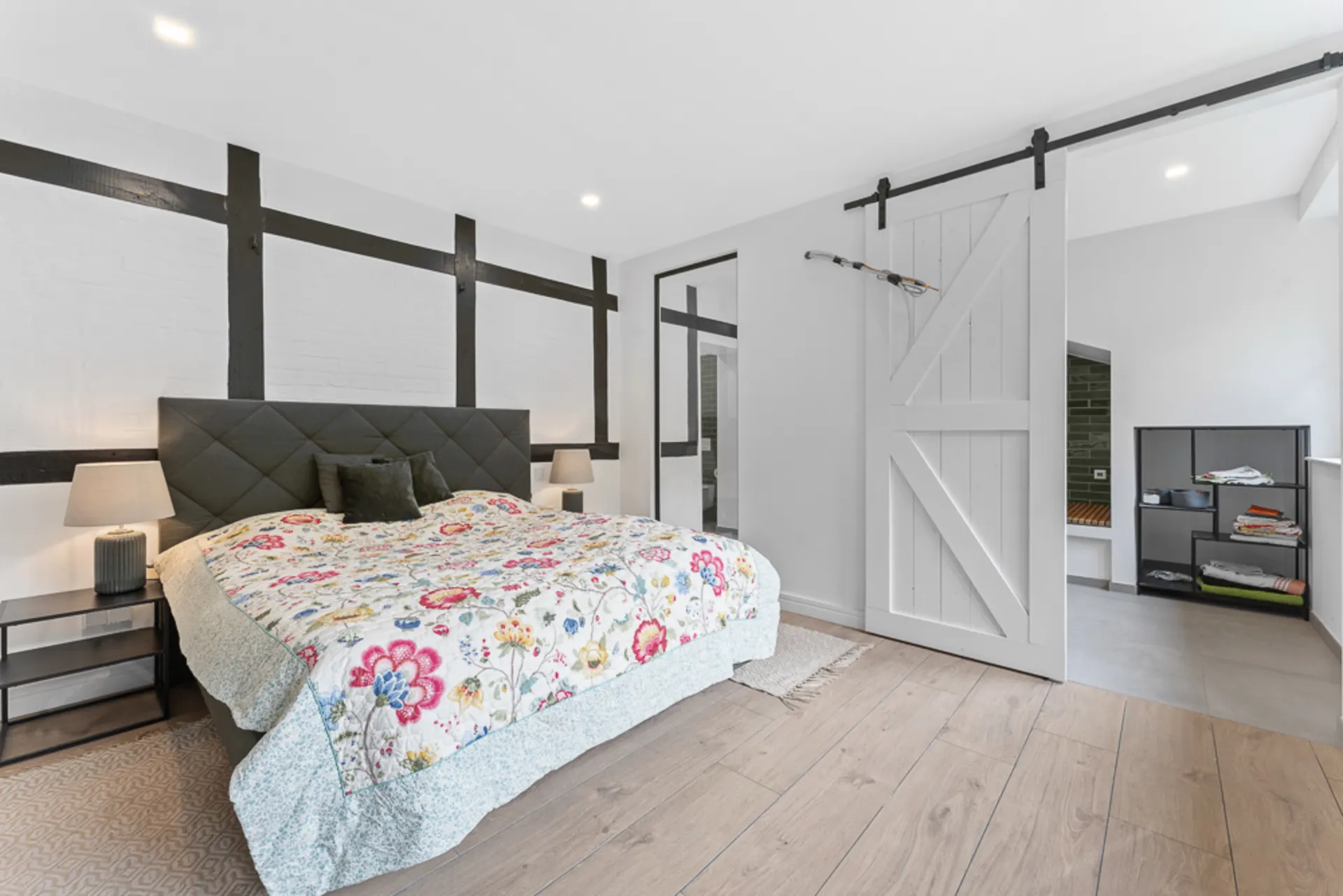 Modernes Schlafzimmer mit Doppelbett, Nachttischen, Schiebetür und Regal im Nebenraum.