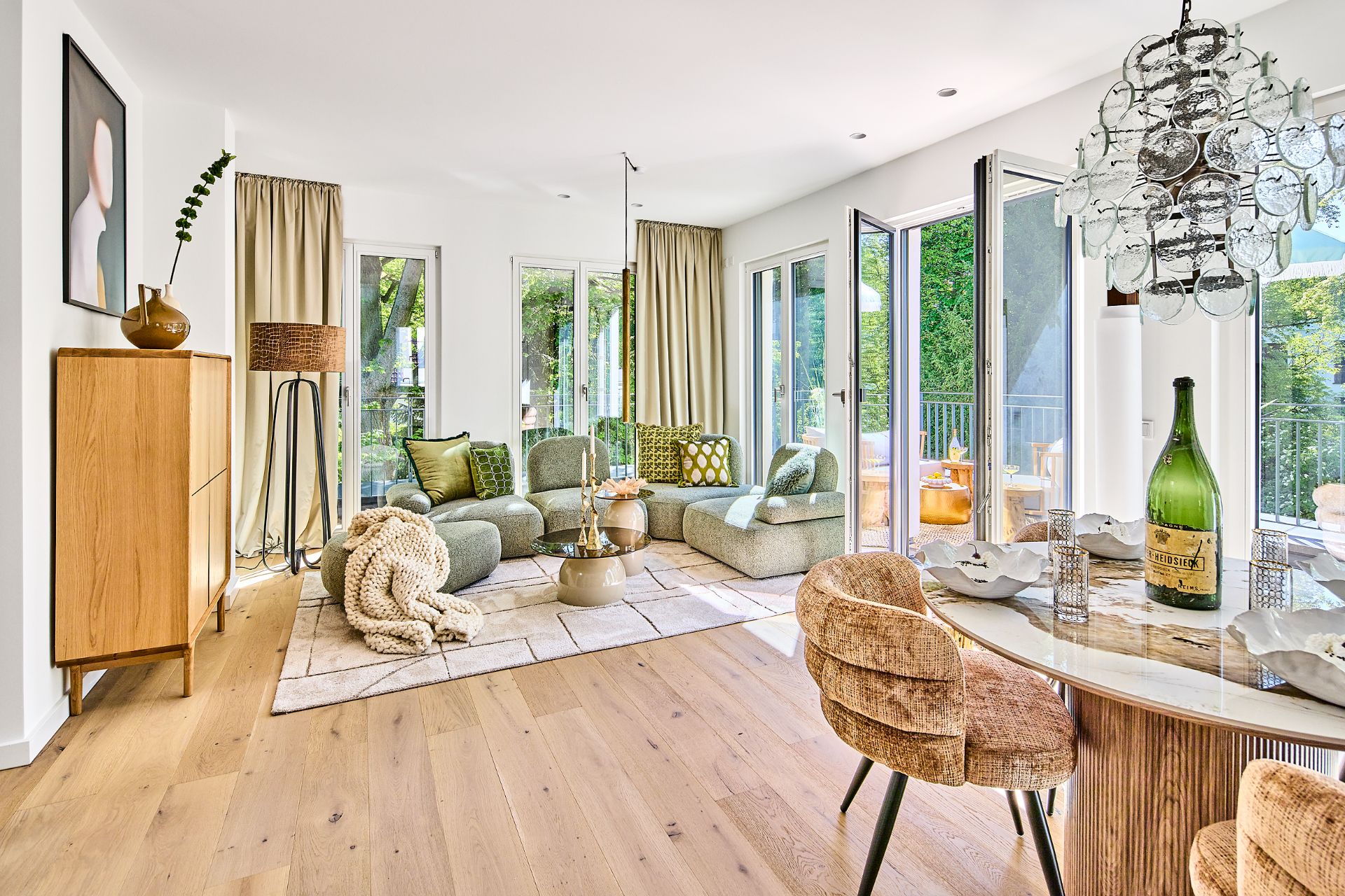 Helles Wohnzimmer mit Sofas, Esstisch, Stühlen, Holzboden und großen Fenstern zum Balkon.