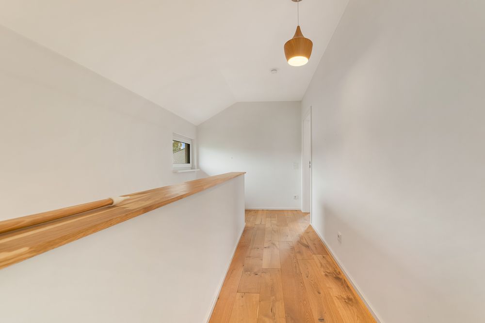 Heller Flur mit Holzfußboden, weißer Wand, Fenster und Holzgeländer.