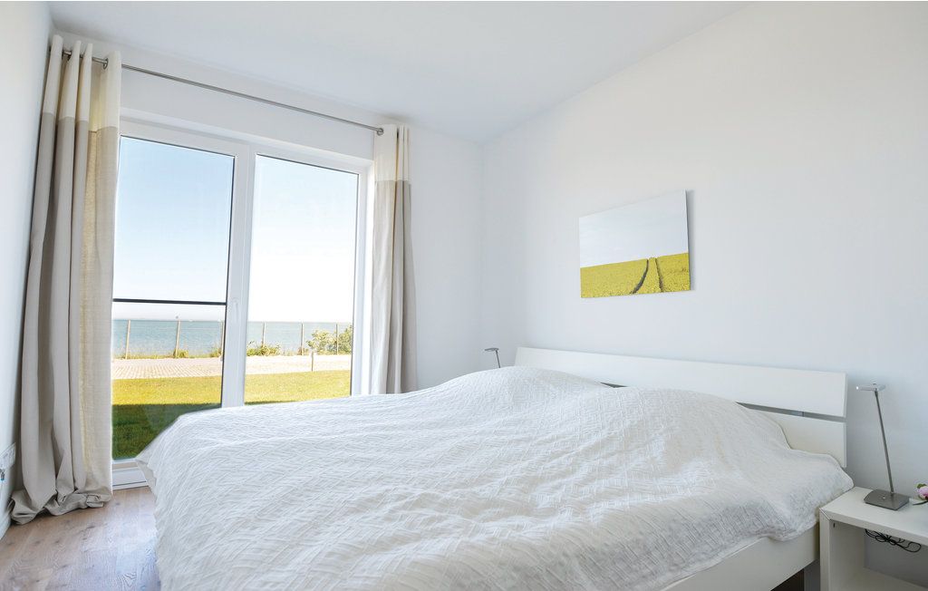 Helles Schlafzimmer mit Doppelbett, weißen Möbeln und großem Fenster mit Blick aufs Meer.