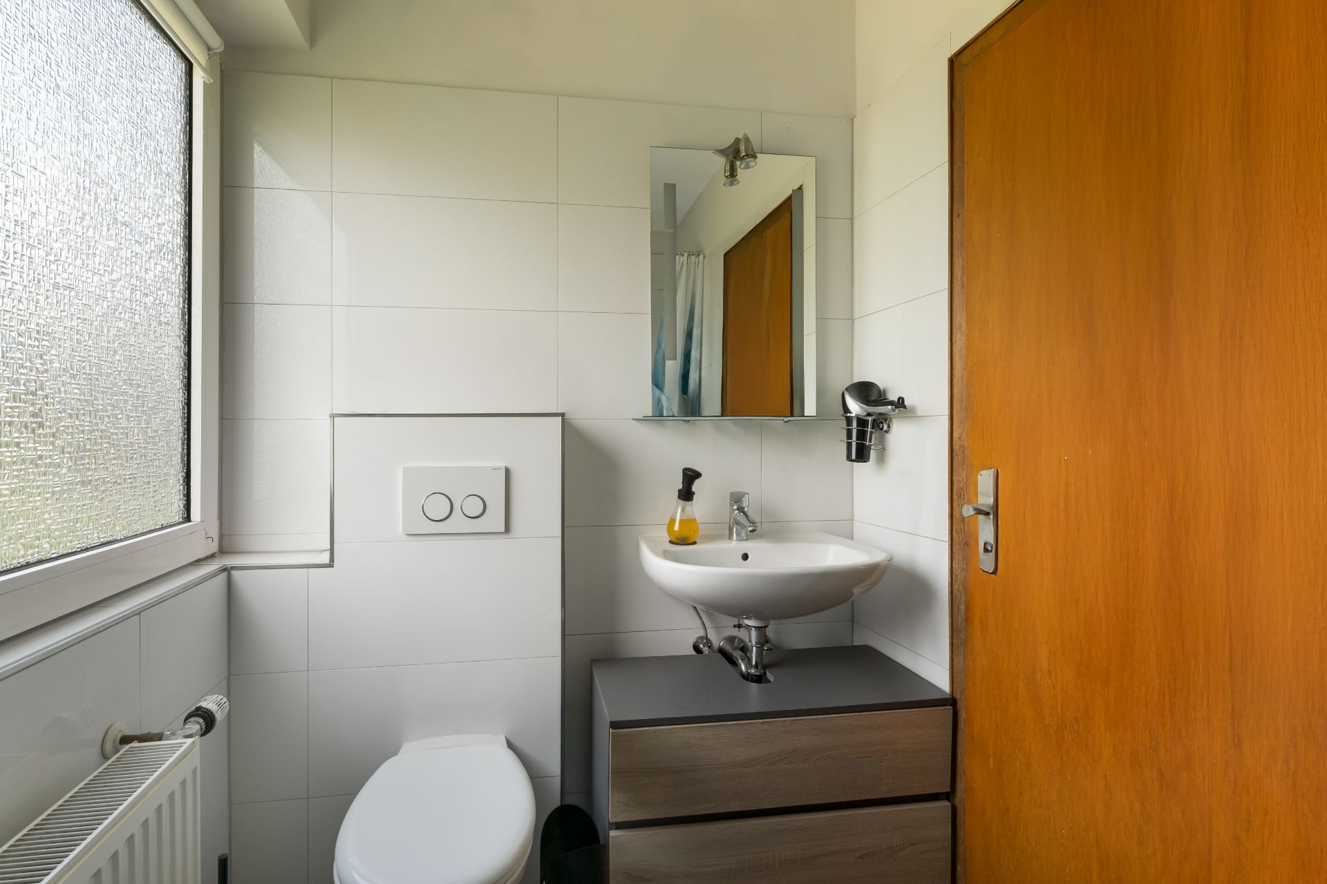 Kleines Badezimmer mit Toilette, Waschbecken, Spiegel und Fenster.