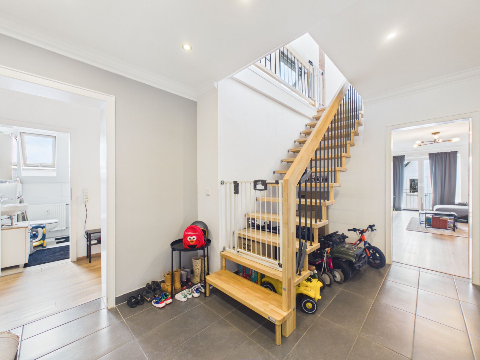 Heller Flur mit Holztreppe, Kinderspielzeug und Schuhen auf dem Boden.
