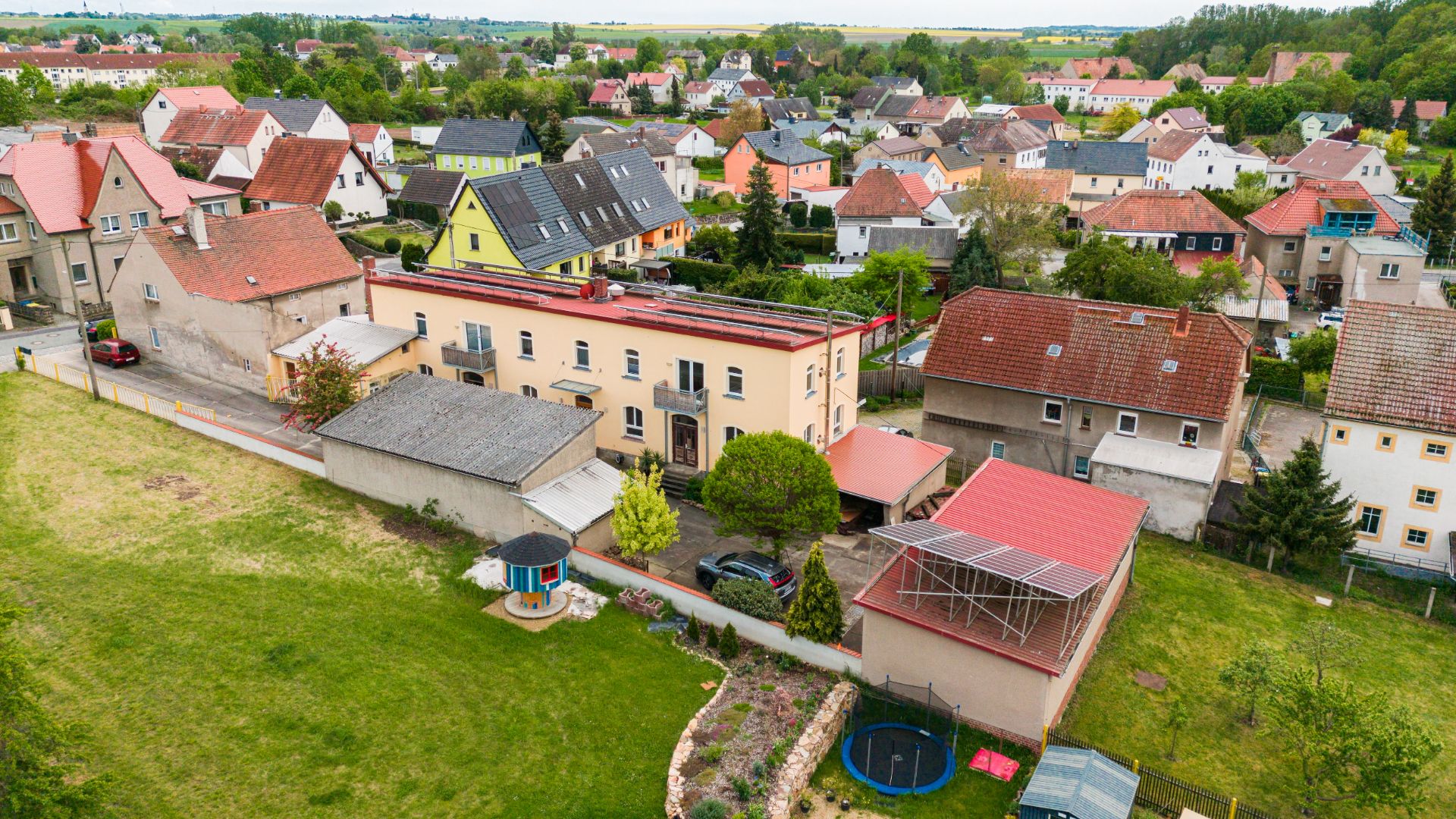 Luftaufnahme eines Wohnhauses mit Garten, Trampolin und mehreren Nachbarhäusern.