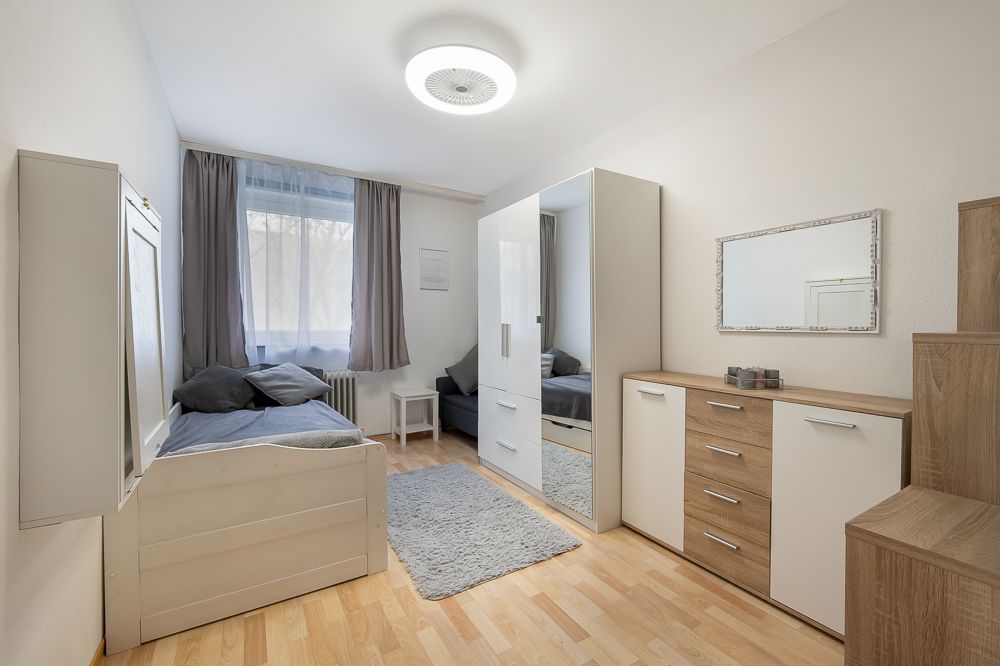 Helles Schlafzimmer mit zwei Betten, Kleiderschrank, Kommode und grauem Teppich.