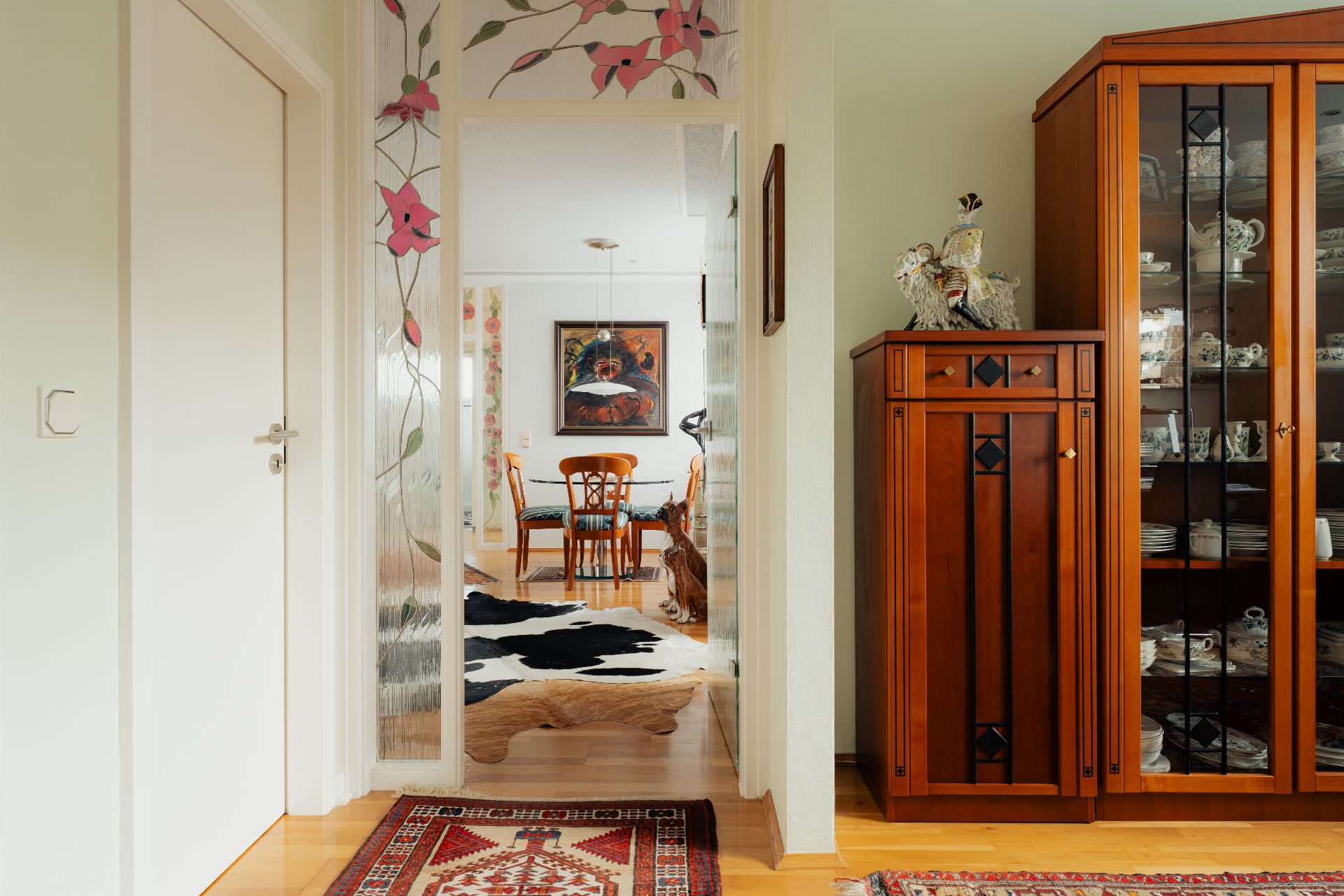 Flur mit Teppich, Blick ins Esszimmer mit Holztisch und Stühlen, Holzvitrine rechts.