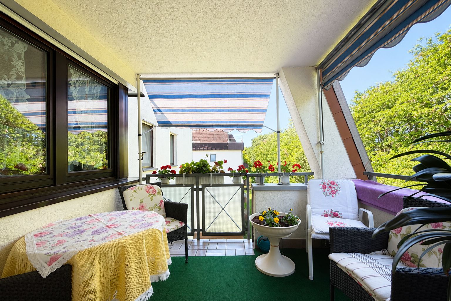 Gemütlicher Balkon mit Sitzmöbeln, Blumen, grünem Teppich und Markise.